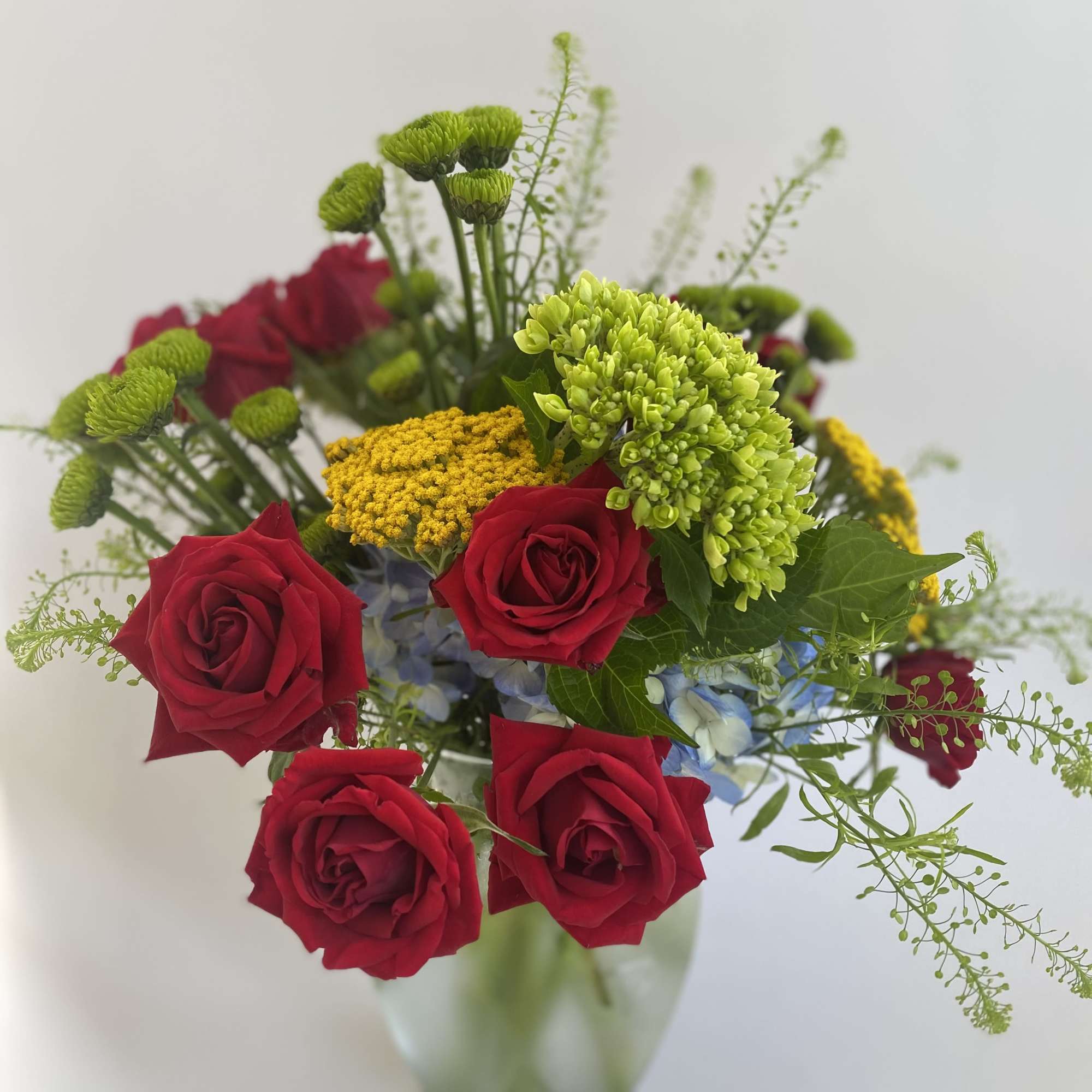 Red roses with green and yellow blooms in a glass vase