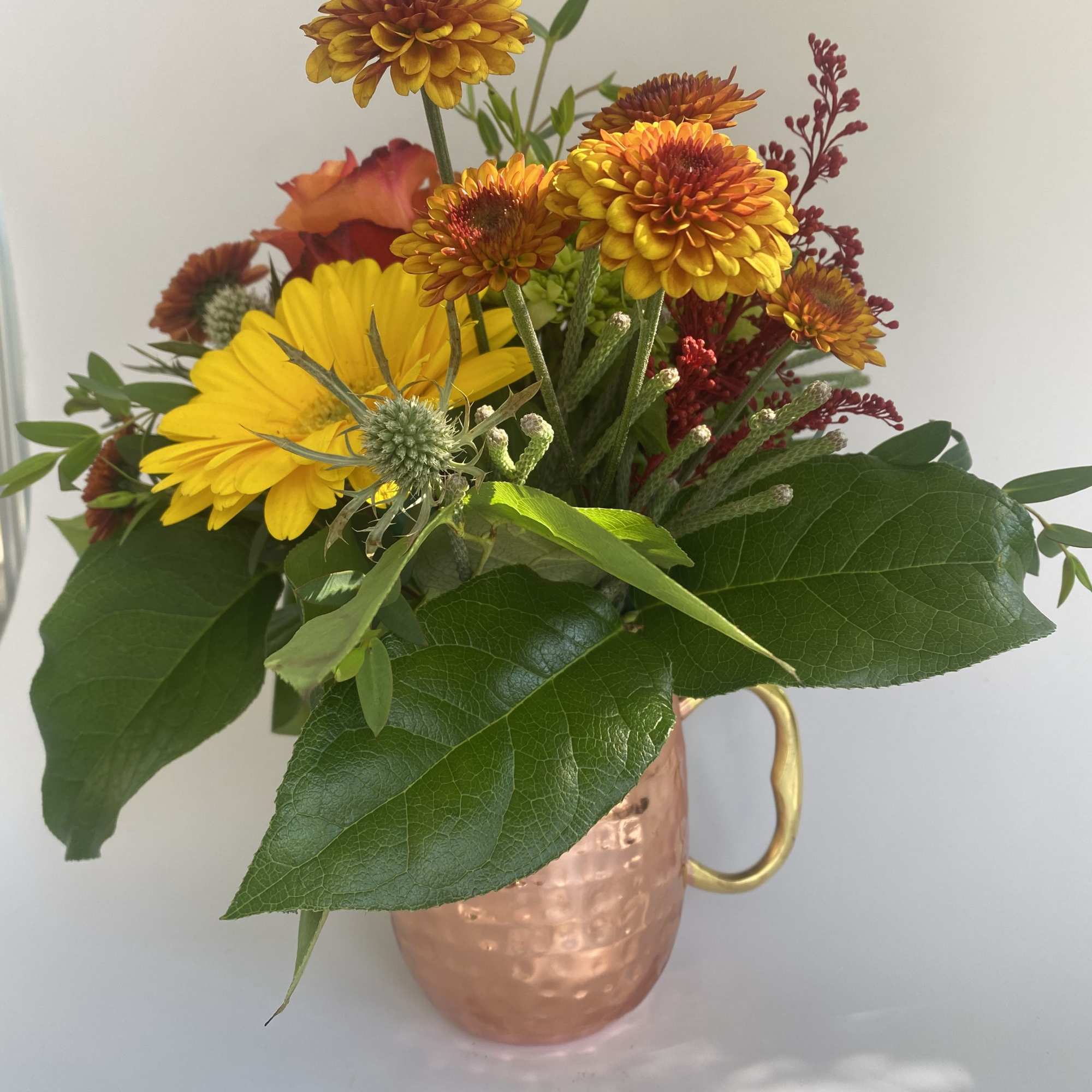 Mixed yellow and orange flowers arranged in a copper mug vase
