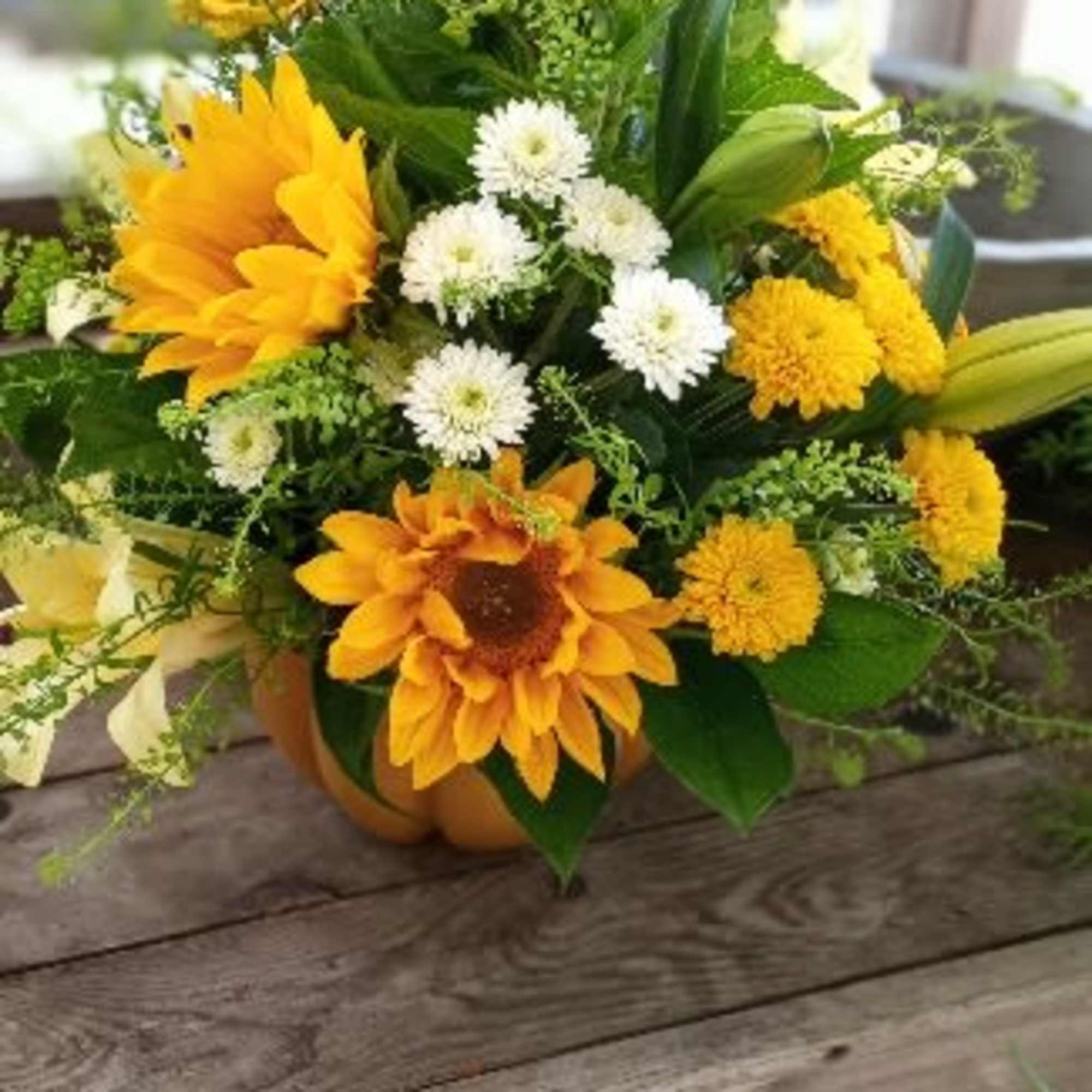 Yellow sunflower and white daisy bouquet in a low pumpkin container
