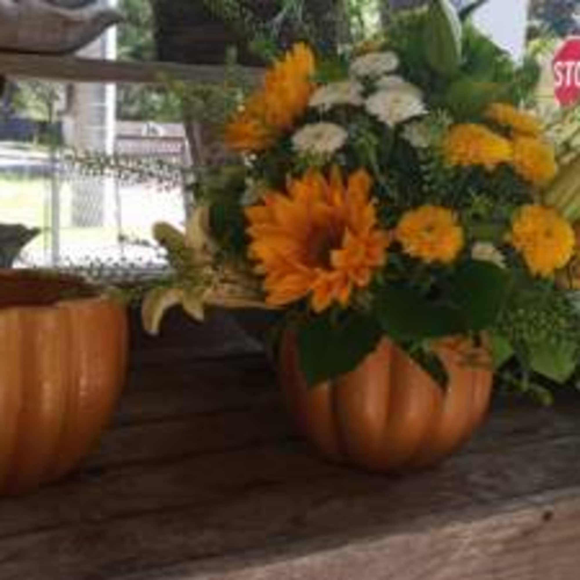 Orange and white floral arrangement in a pumpkin-shaped container beside an empty pumpkin pot.