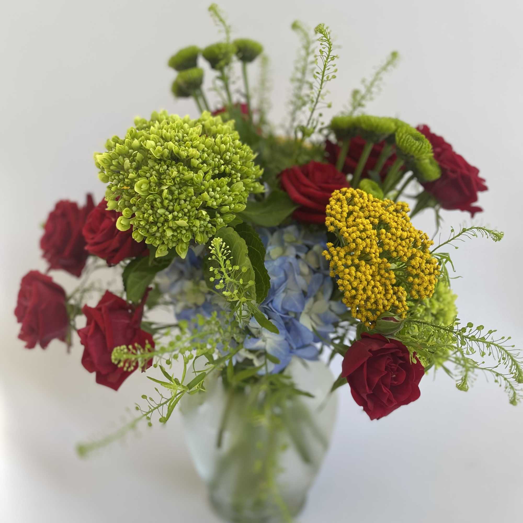 Mixed bouquet of red roses, blue hydrangea, and green blooms in a glass vase