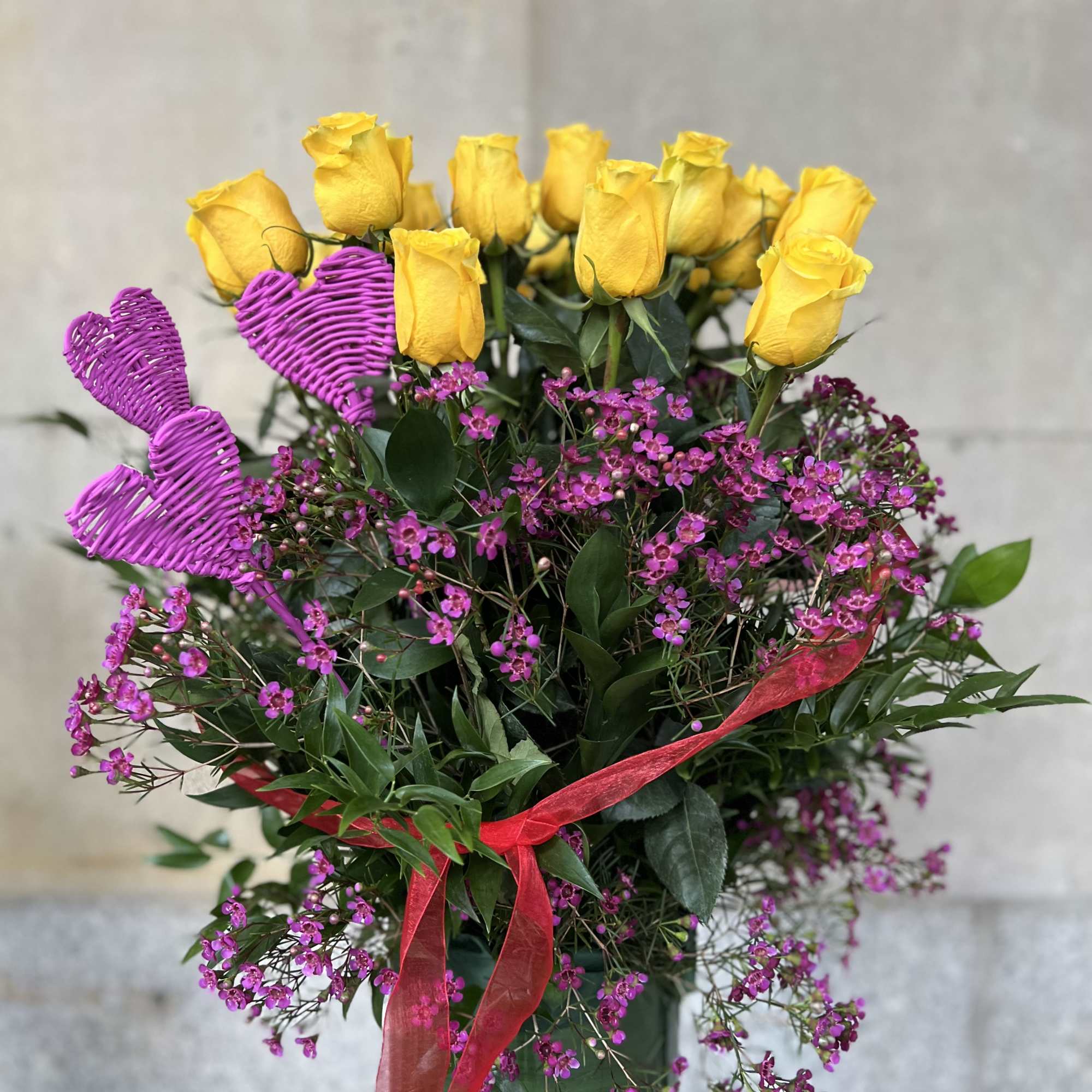 Yellow roses with pink filler flowers in a glass vase and heart picks
