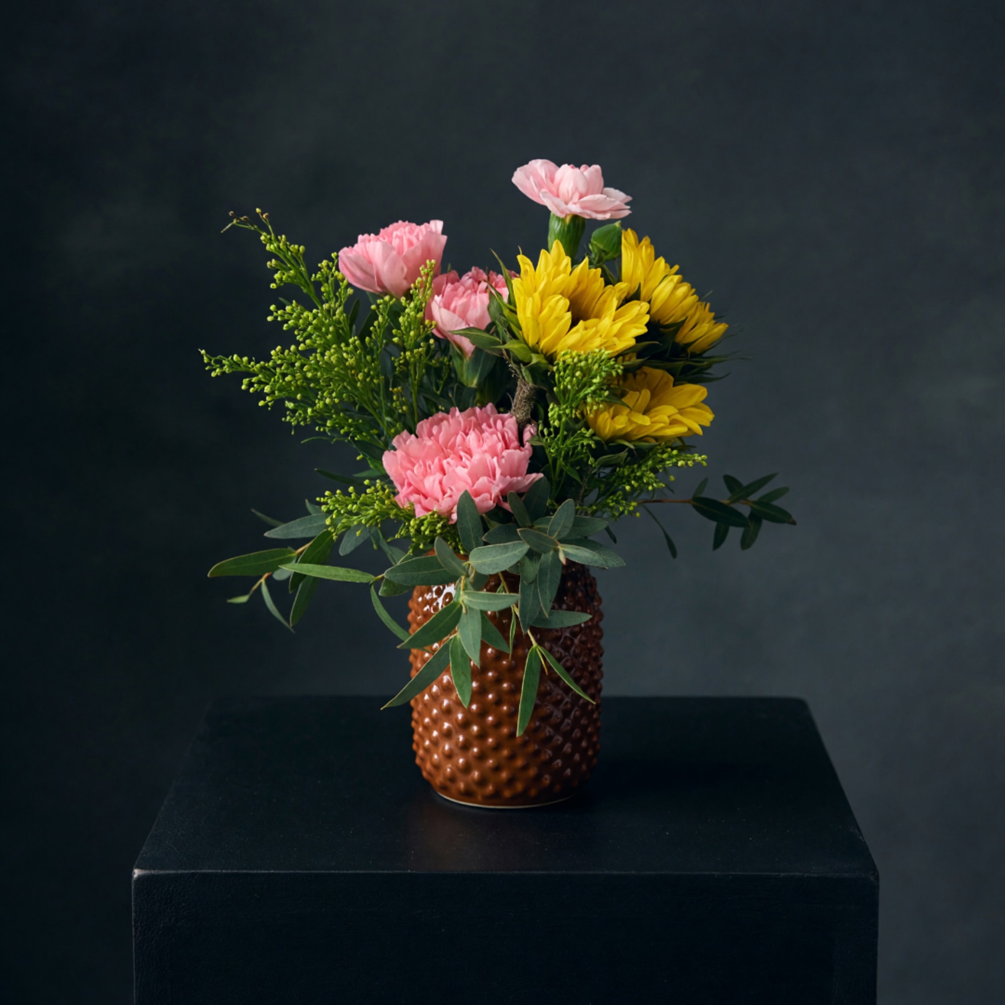 Pink and yellow flowers arranged in a textured brown vase