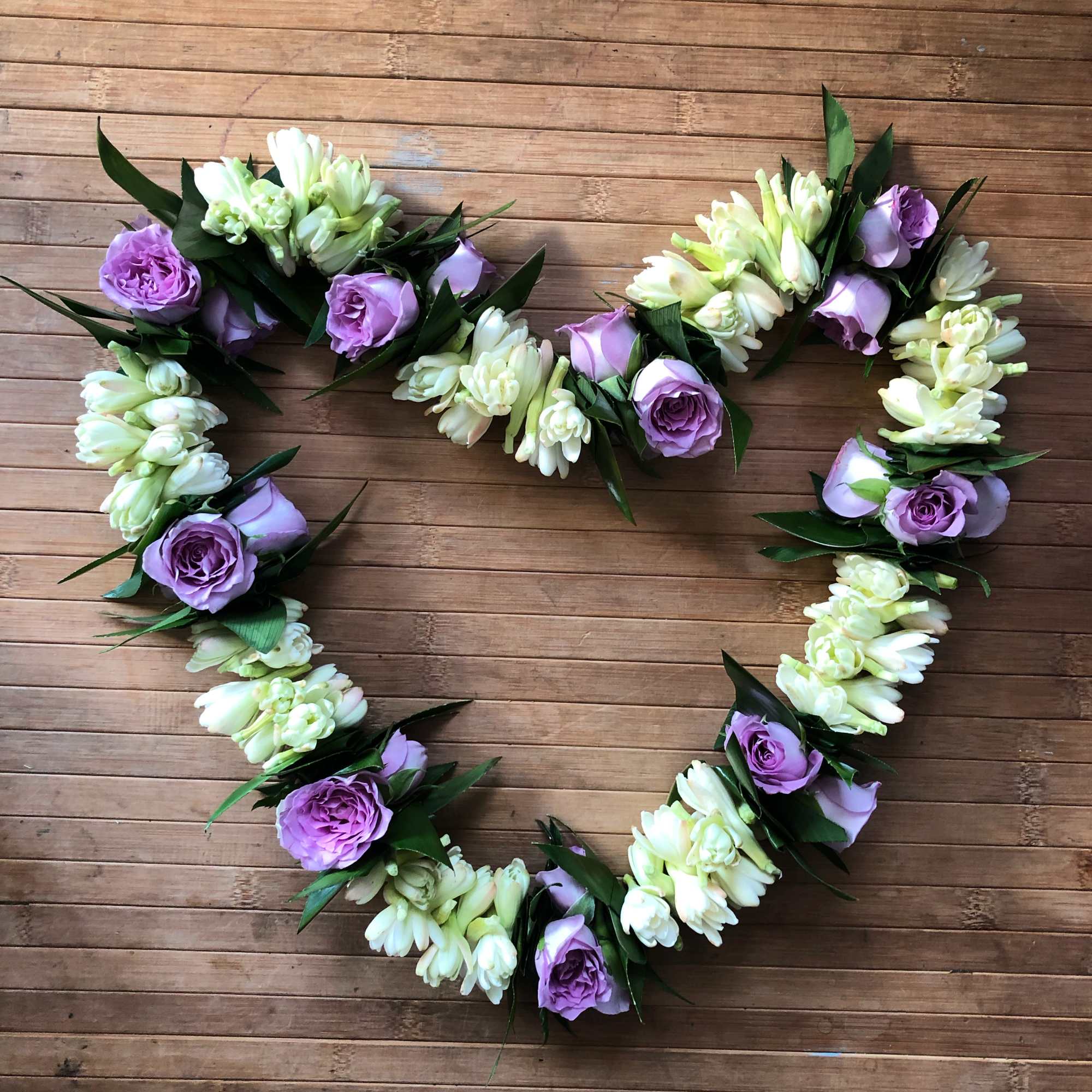 Heart-shaped floral garland with purple roses and white blossoms on wood