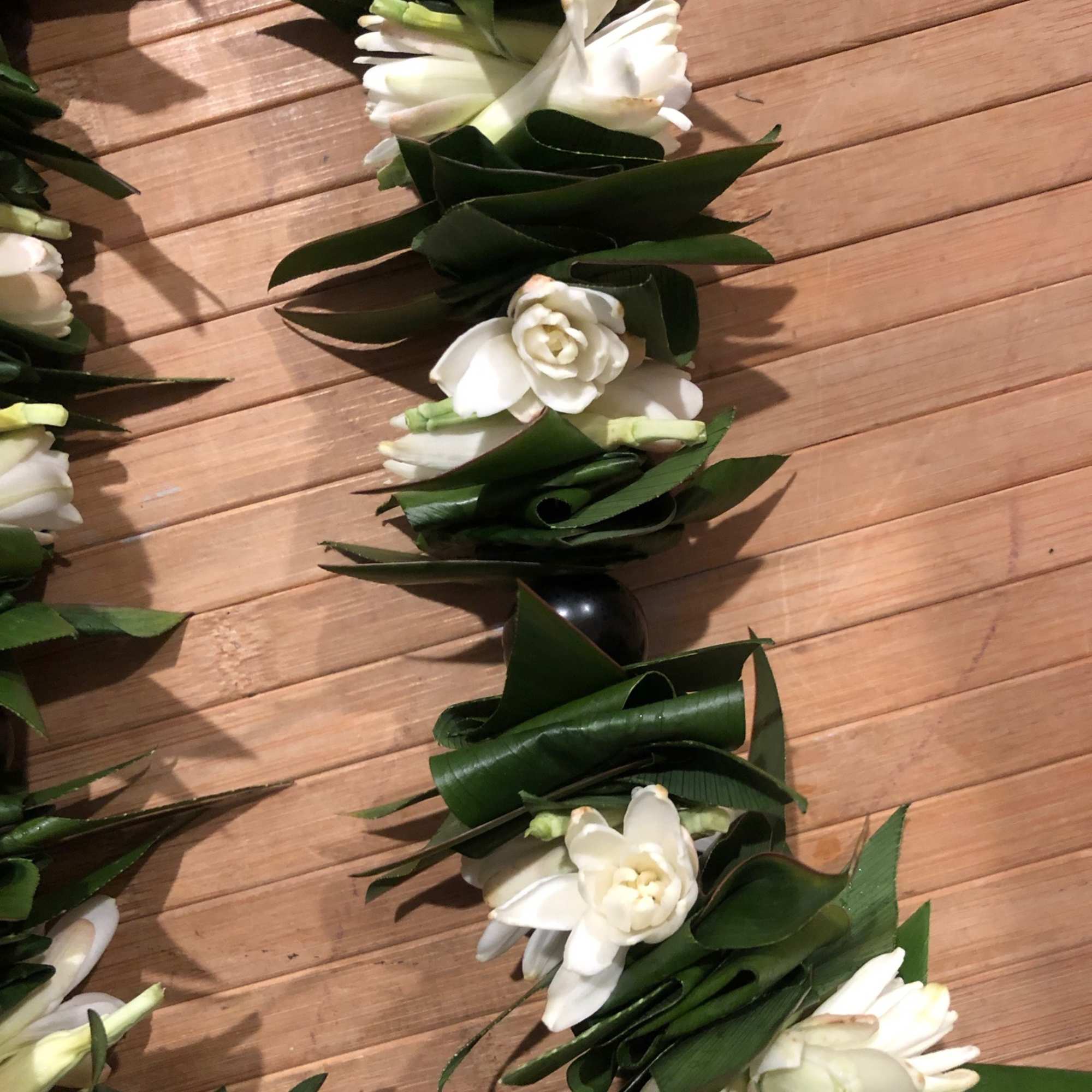 White floral garland with dark green leaves on a wooden floor