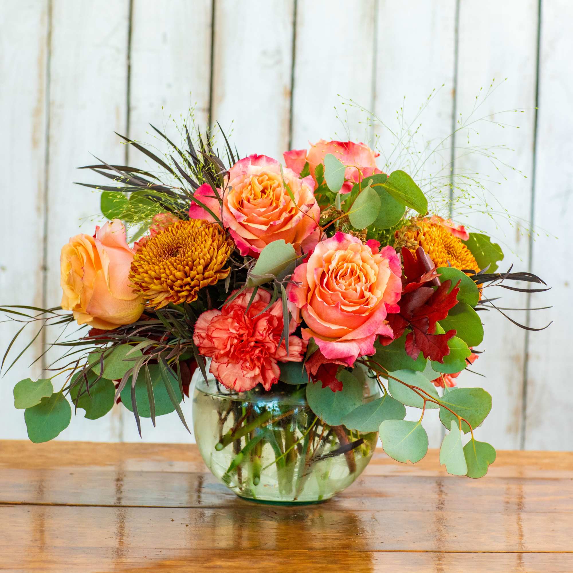 Mixed bouquet of peach roses and orange mums in a glass vase