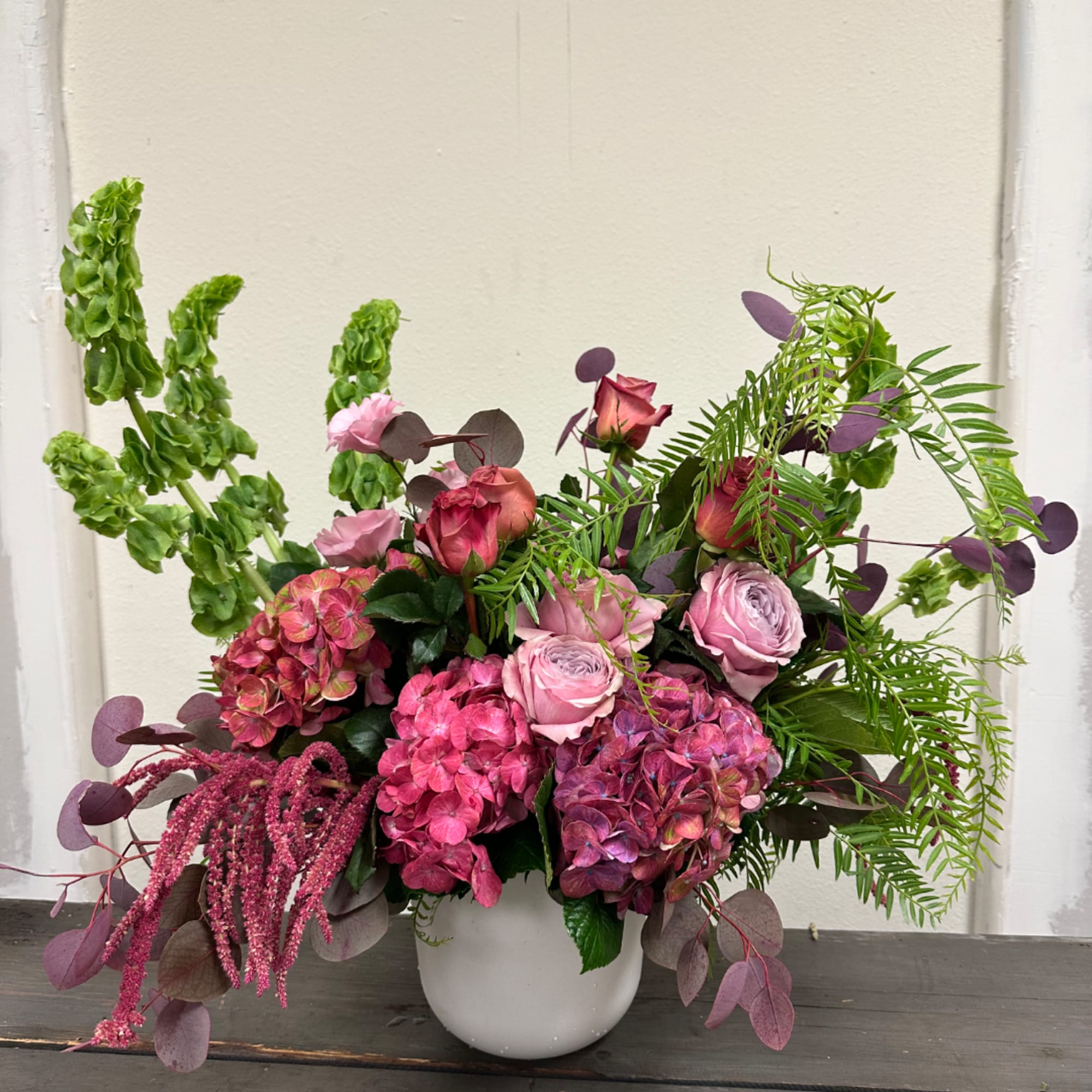 Pink roses and hydrangeas arranged in a white vase with green and purple foliage
