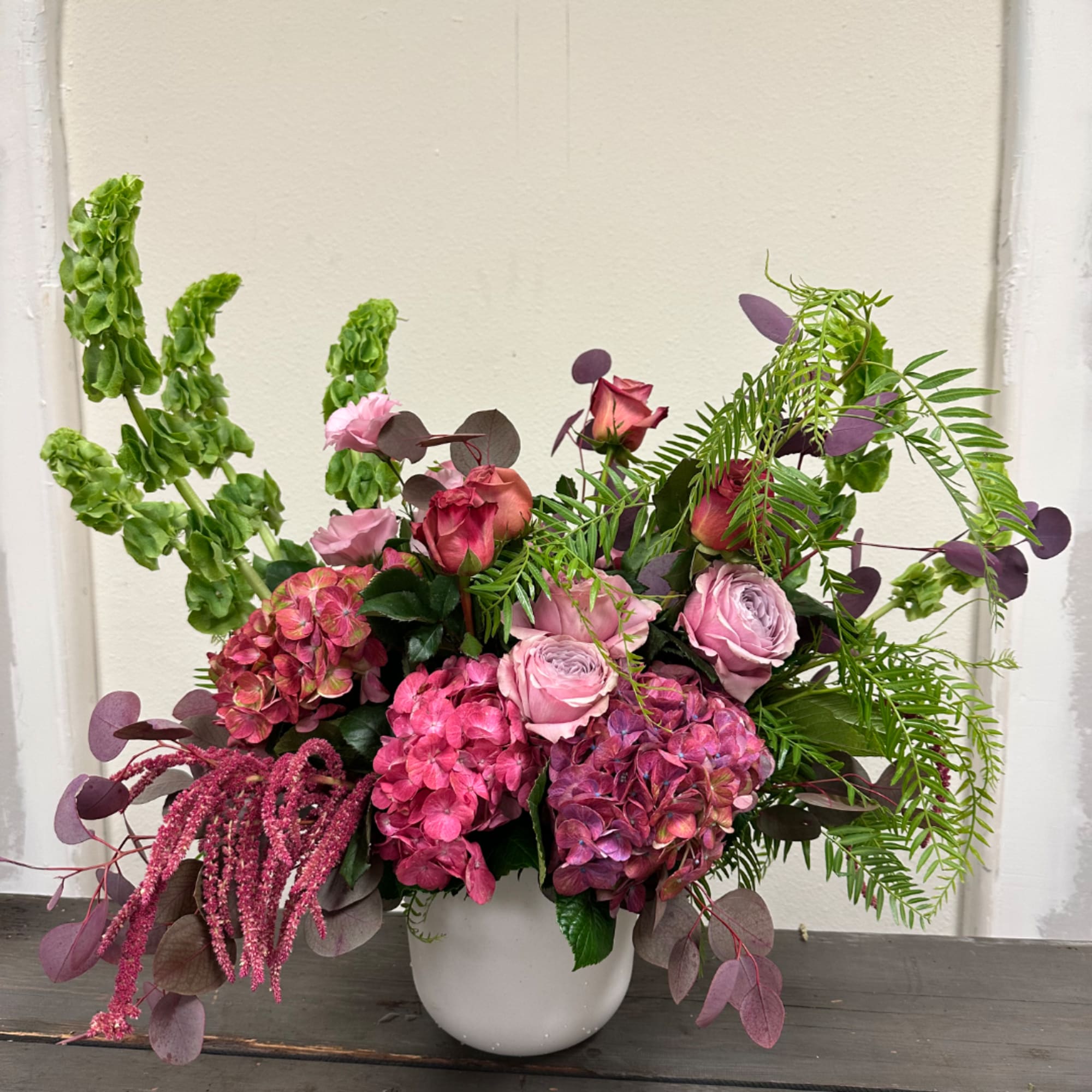 Pink and purple floral arrangement in a white vase with trailing greenery