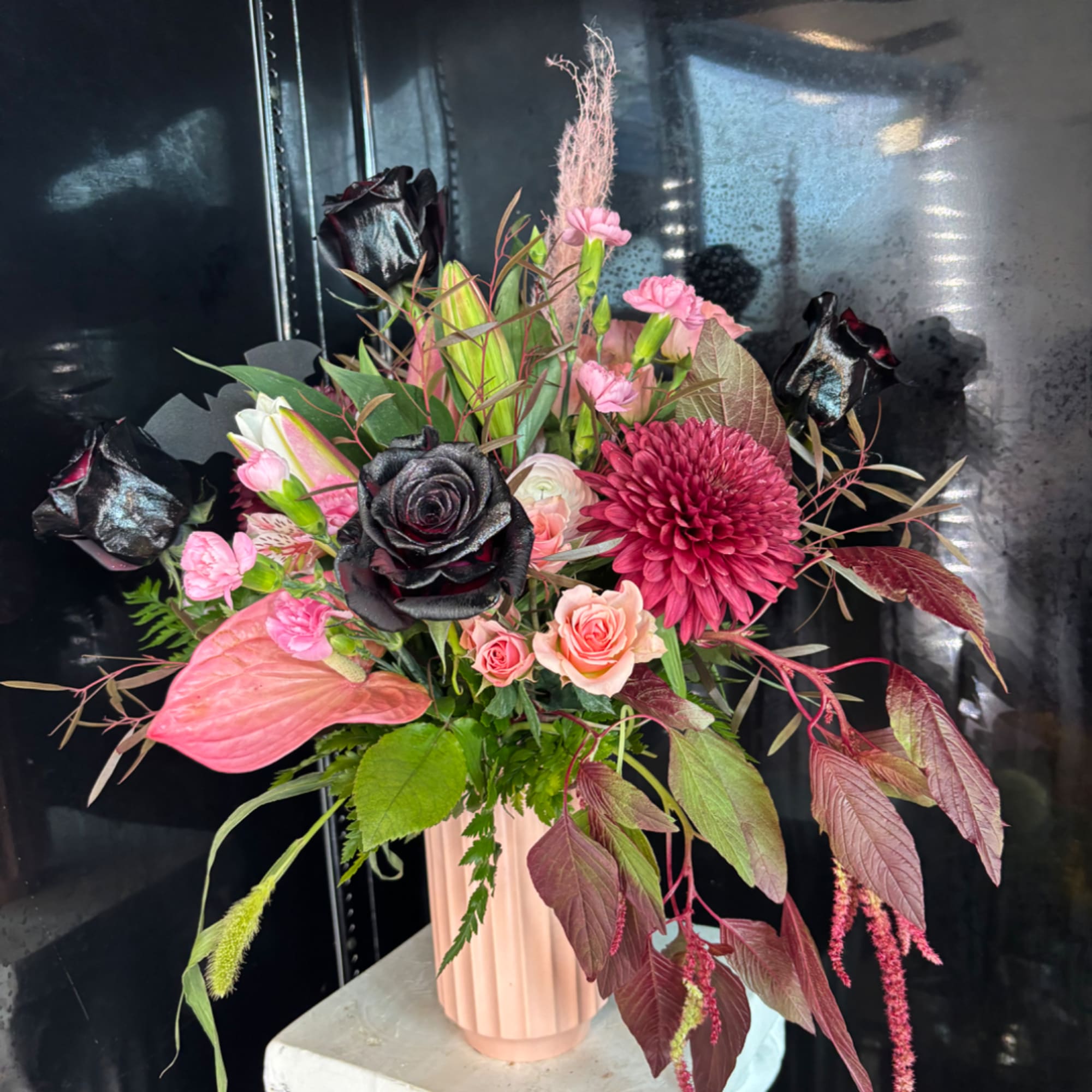 Pink and burgundy floral arrangement in a blush vase with black roses
