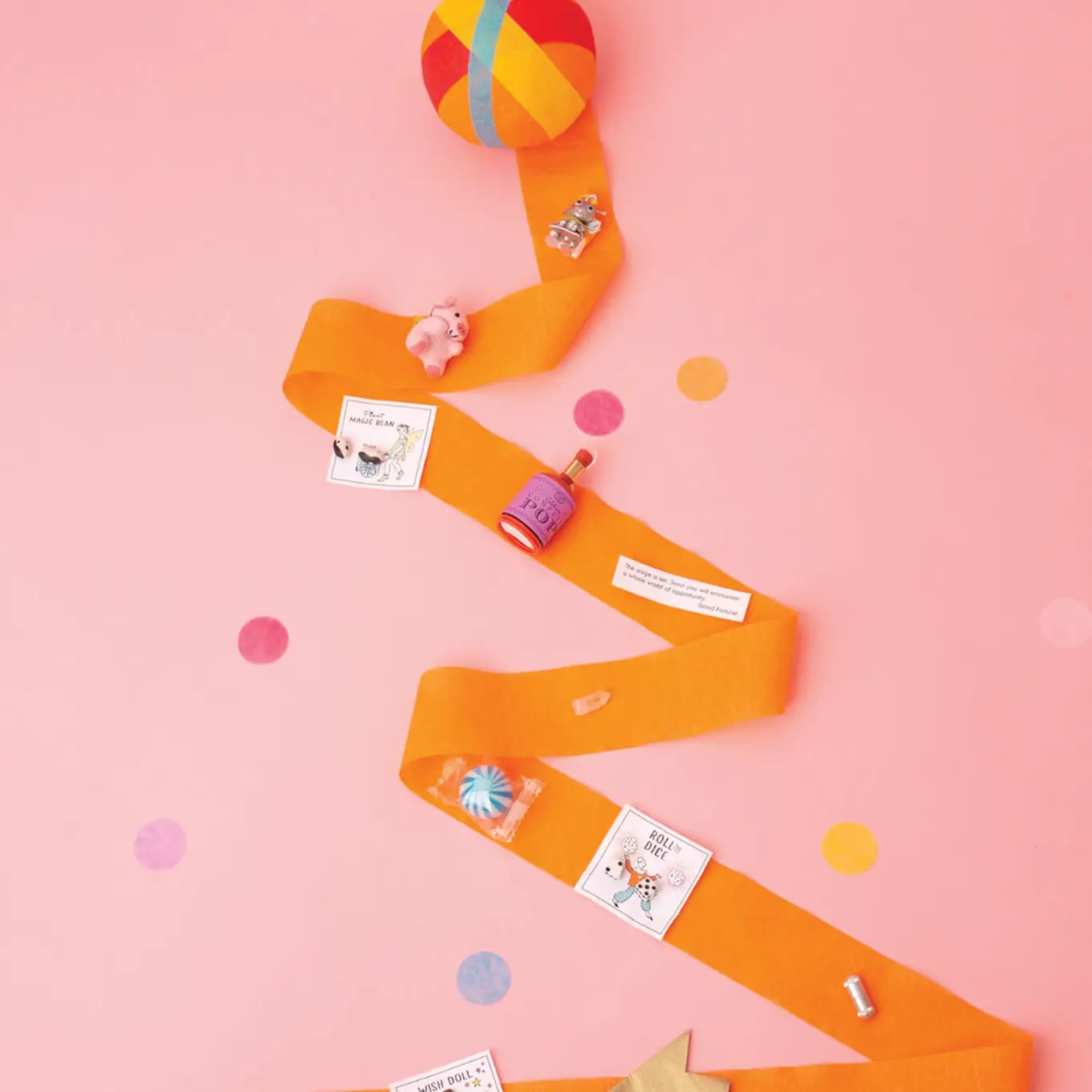 Orange ribbon arranged like a tree with small gift items on a pink background