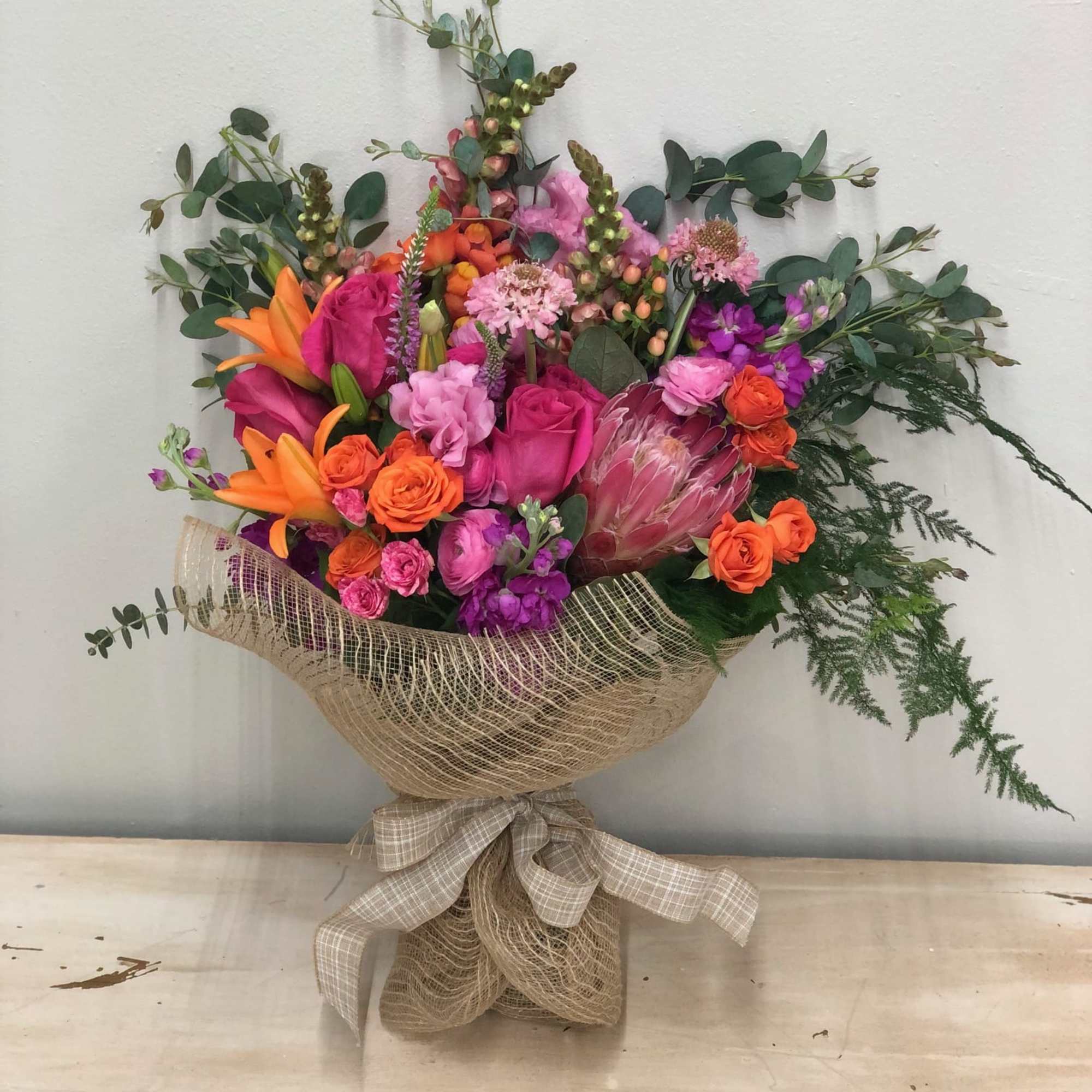 Bright mixed bouquet with pink, orange, and purple flowers wrapped in burlap
