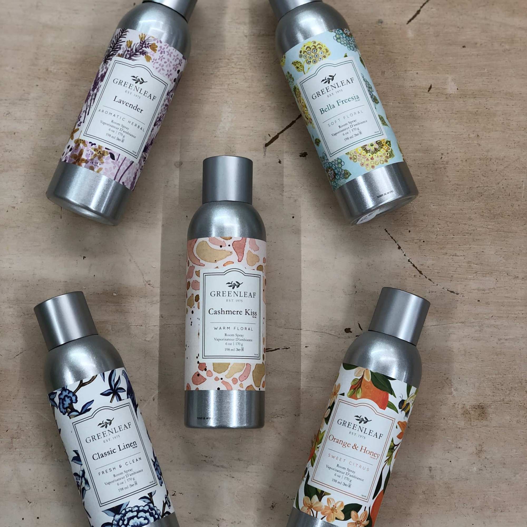 Set of five Greenleaf scented room spray bottles arranged on a wood surface