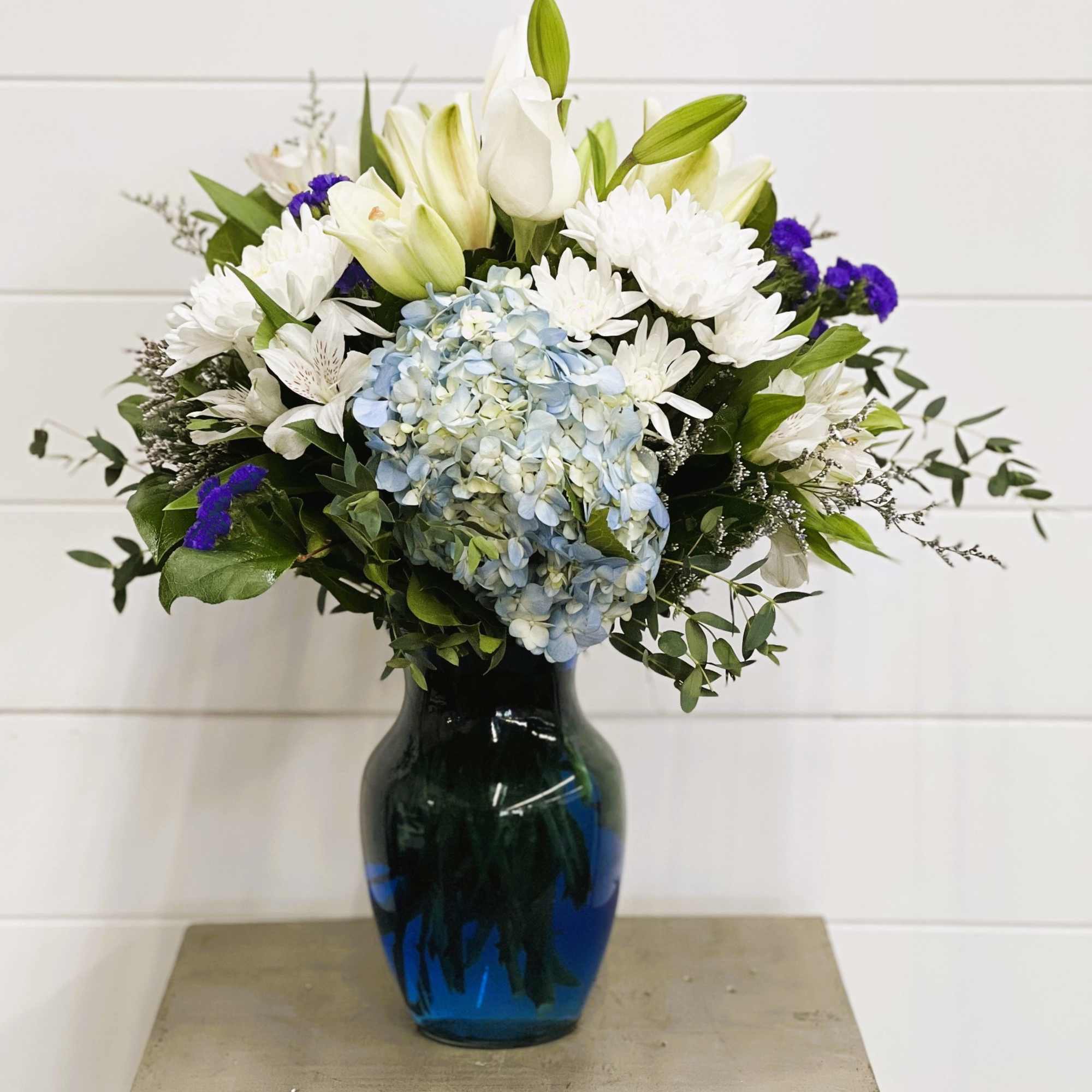 White lilies and daisies with blue hydrangea in a blue vase