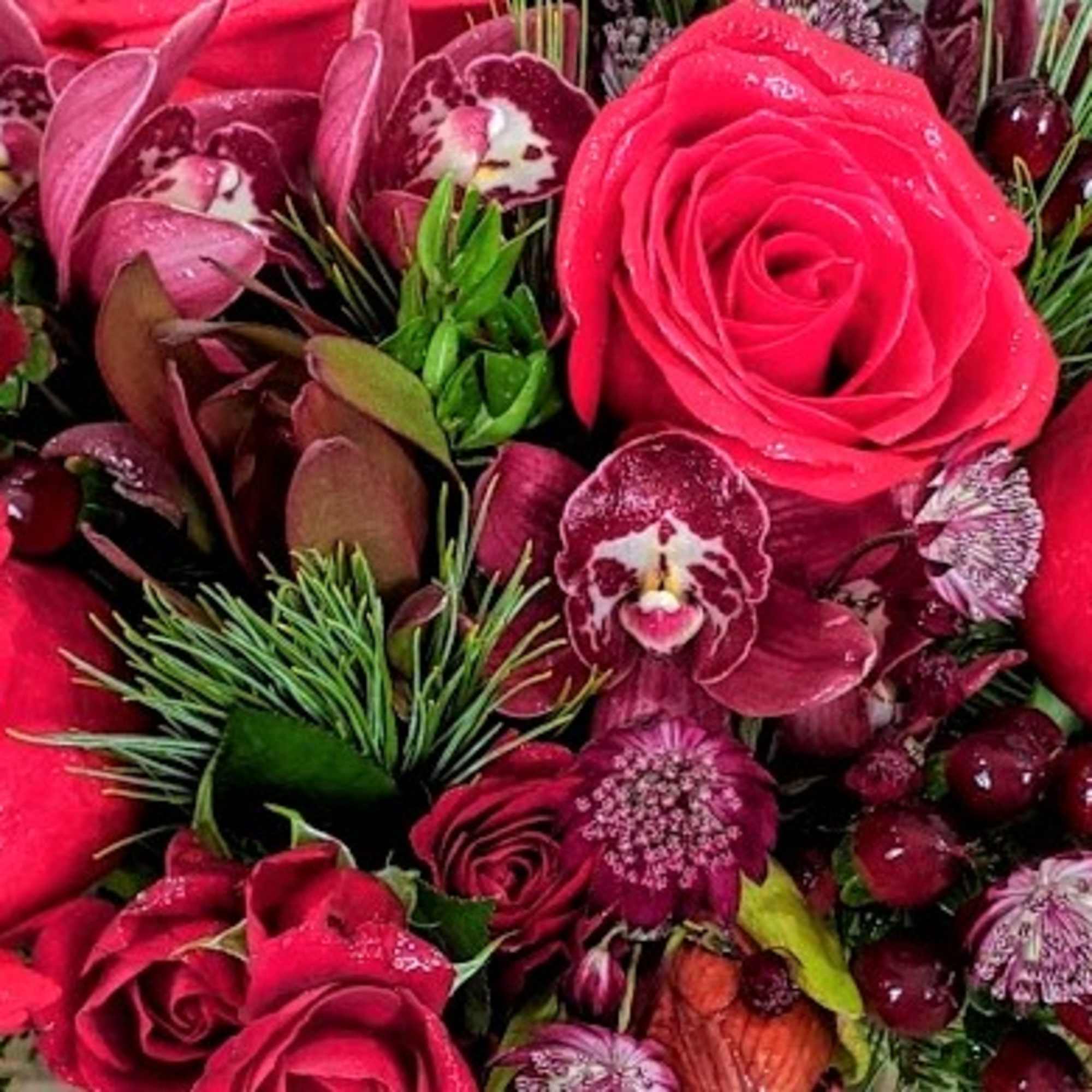 Close-up of a rich red bouquet with roses, orchids, berries, and pine accents