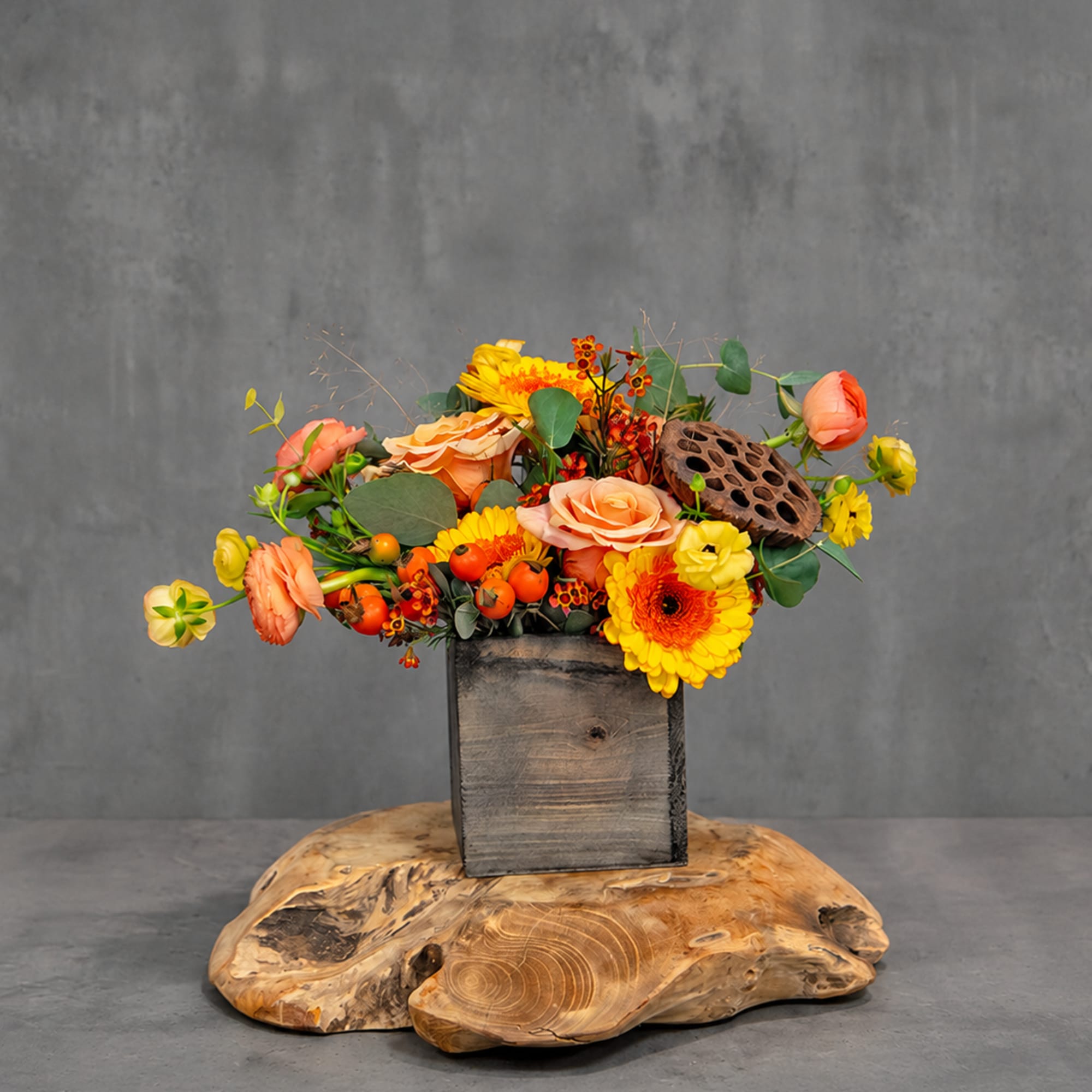 Orange and yellow floral arrangement in a wooden box on a wood slab