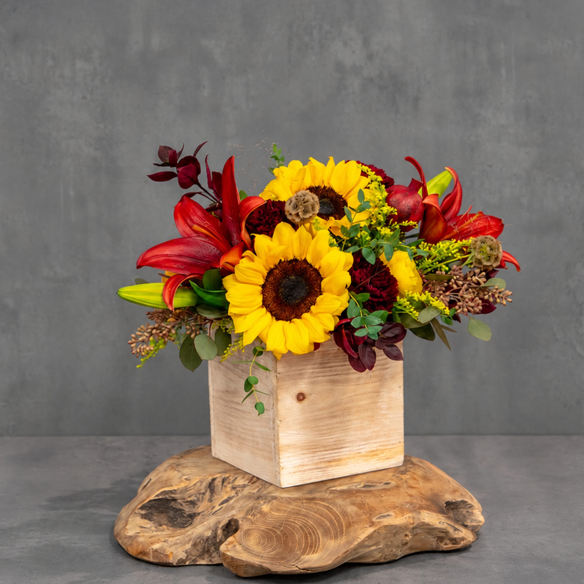 Sunflower and red lily arrangement in a wooden box on a wood slab