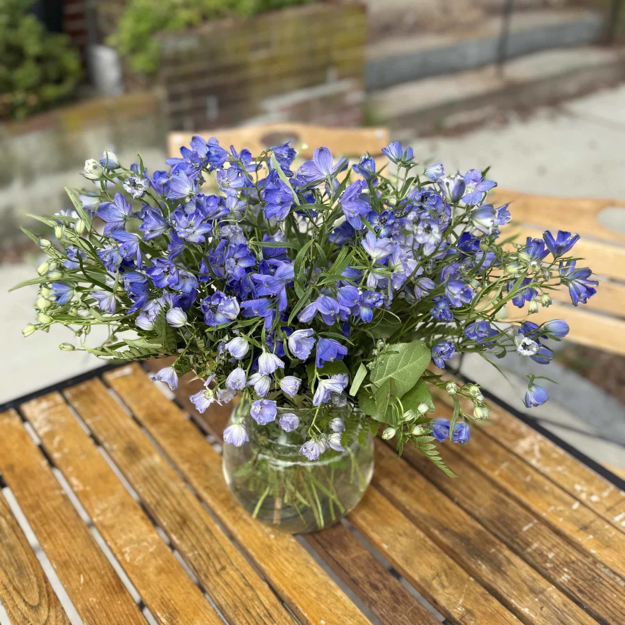 Blue wildflower bouquet in a clear glass vase on a wooden table
