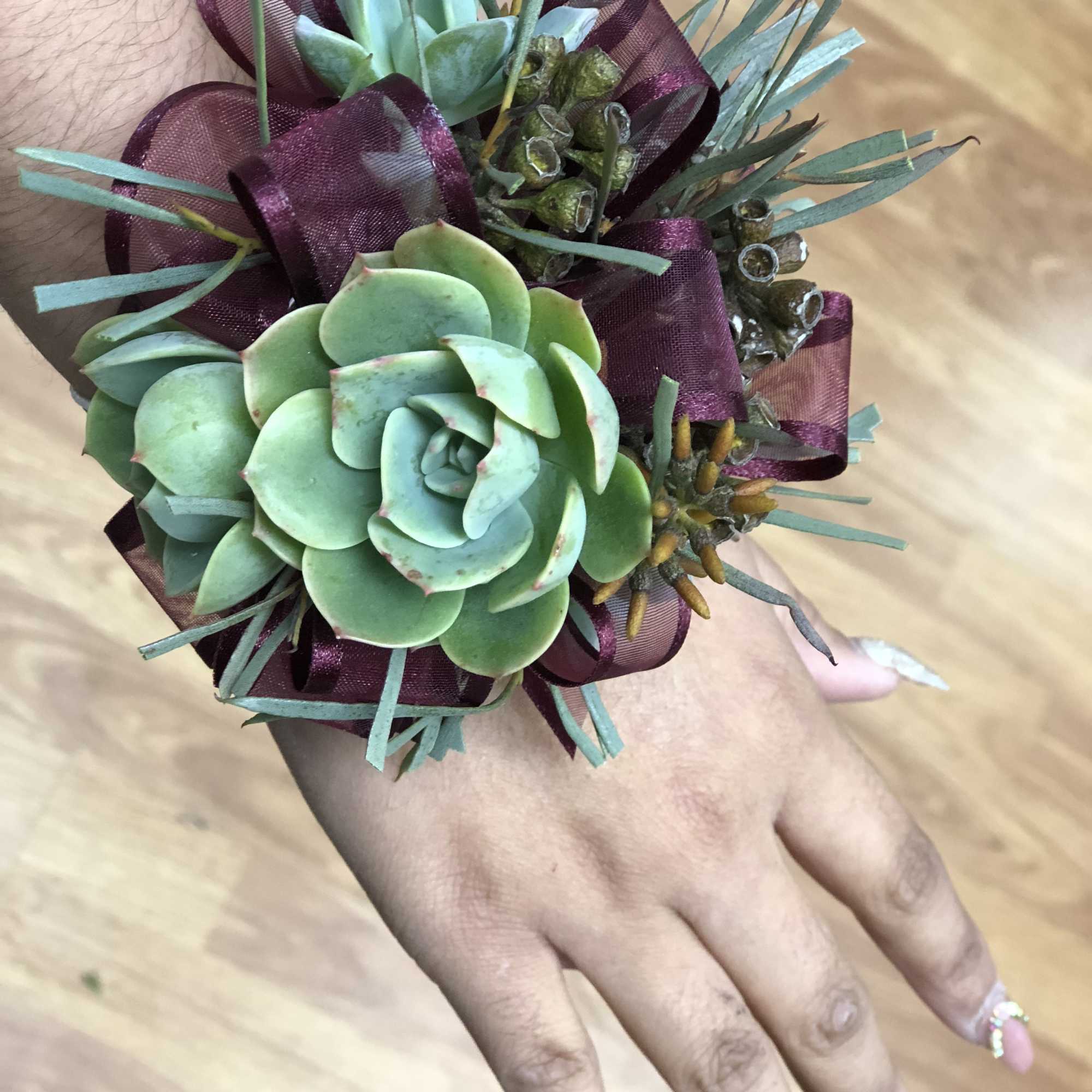 Succulent wrist corsage with burgundy ribbon on a hand