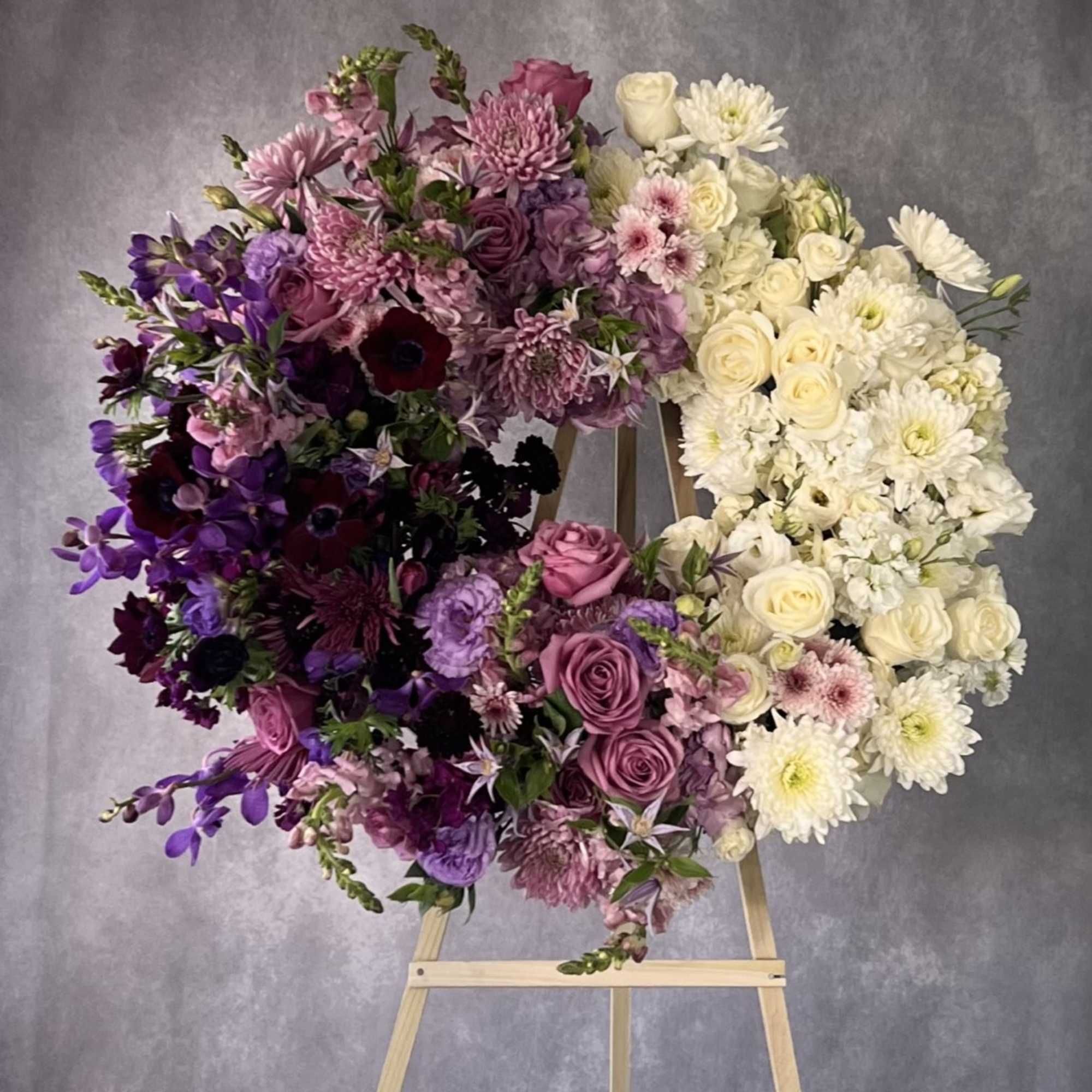 Heart-shaped floral wreath in purple, pink, and white on a wooden easel
