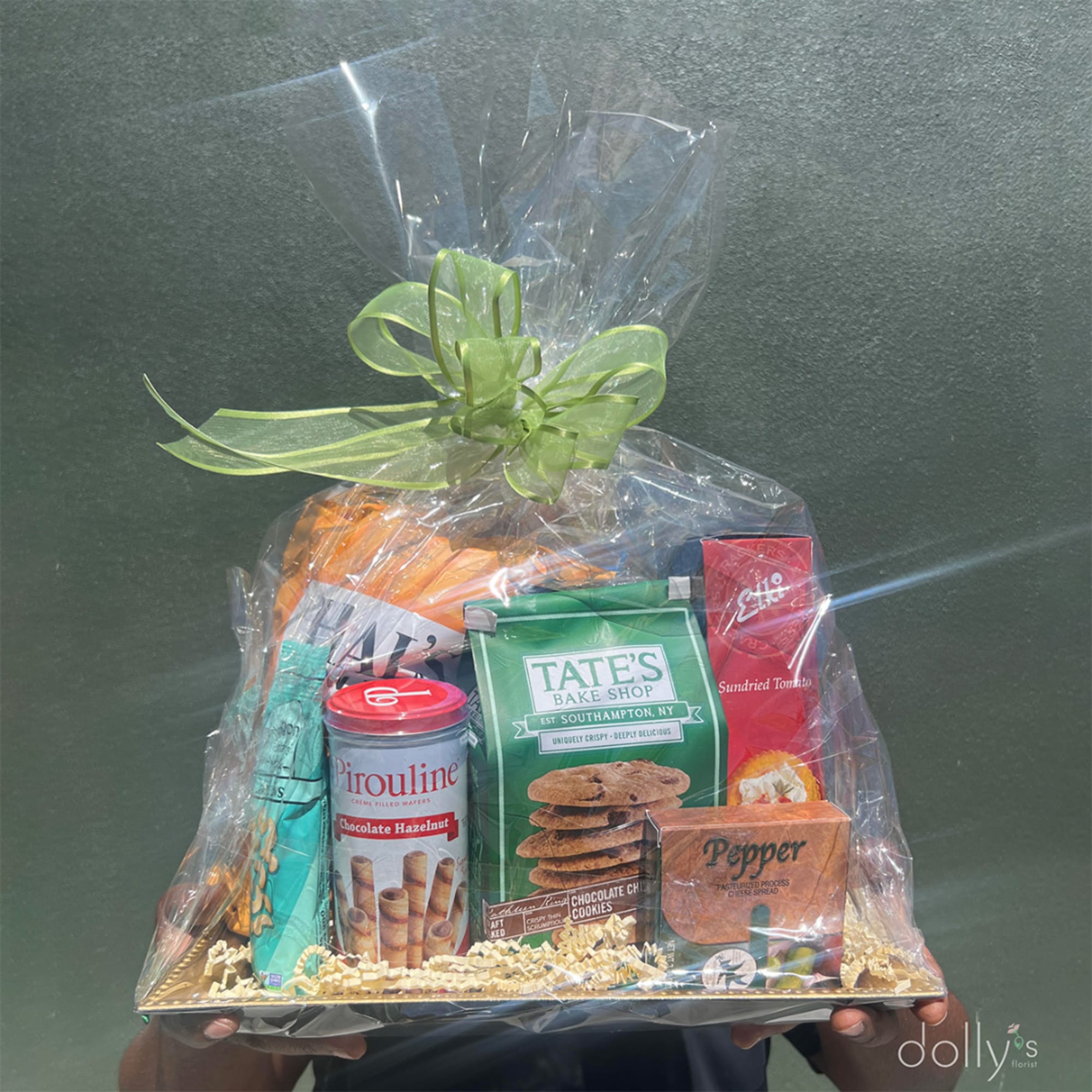 Gift basket of assorted snacks wrapped in clear cellophane with a green bow