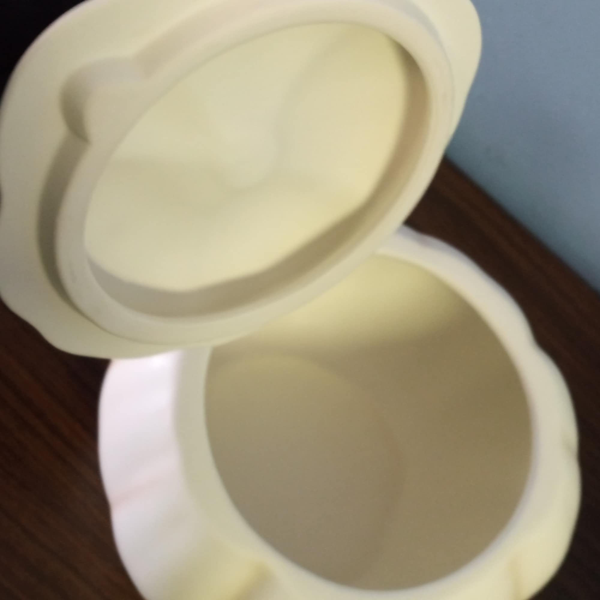 Two cream-colored ceramic containers with lids on a wooden surface