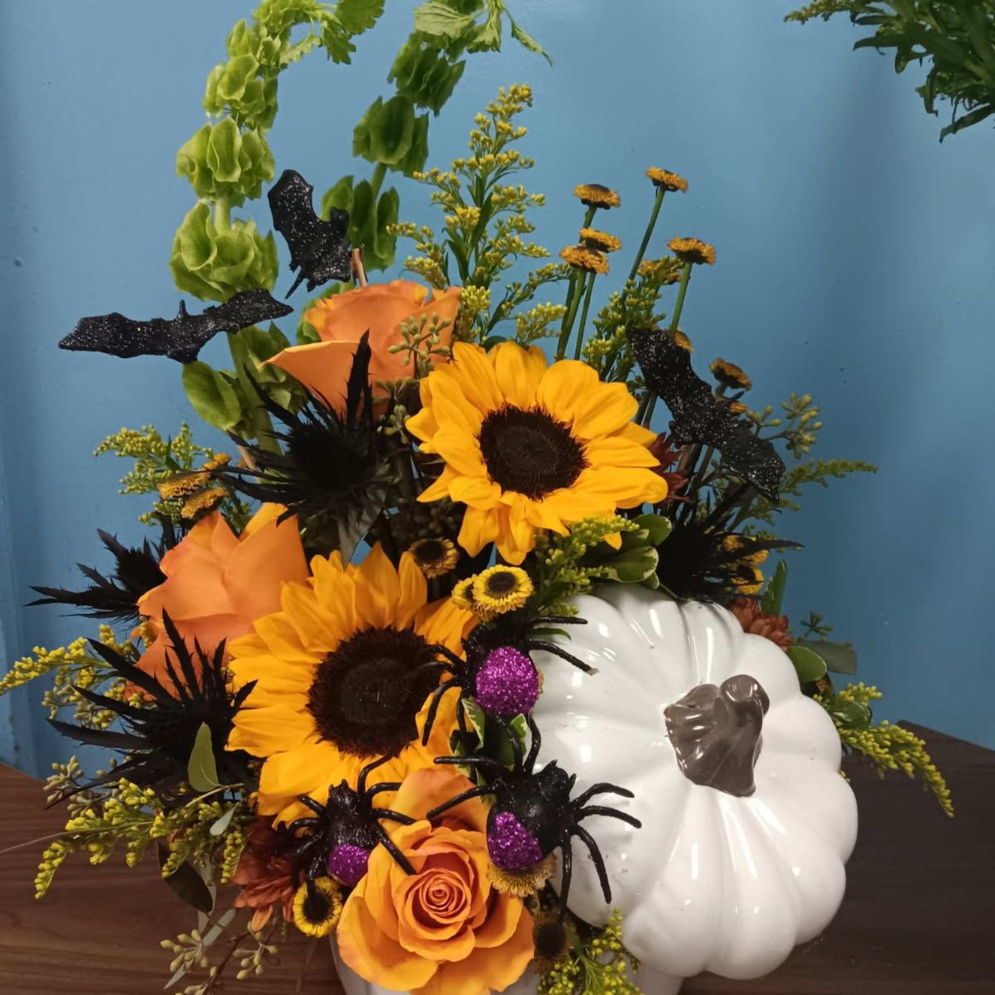 Orange and yellow floral arrangement in a white pumpkin container with black spider decorations