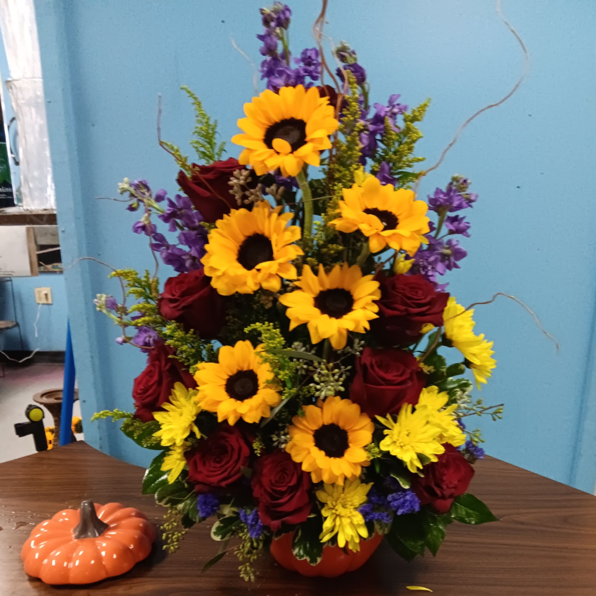 Tall mixed bouquet with sunflowers, red roses, and yellow daisies in a pumpkin container