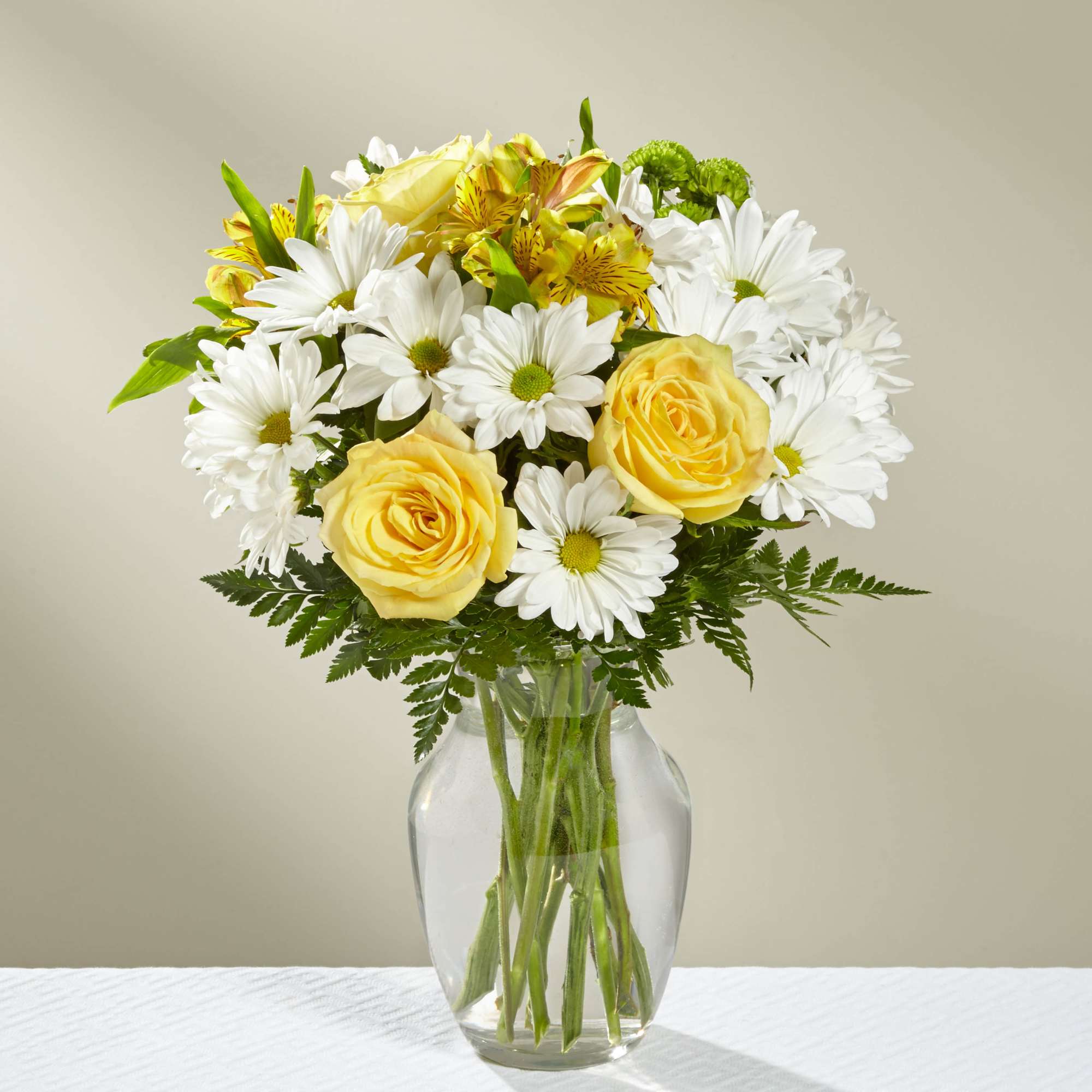 Yellow roses and white daisies in a clear glass vase