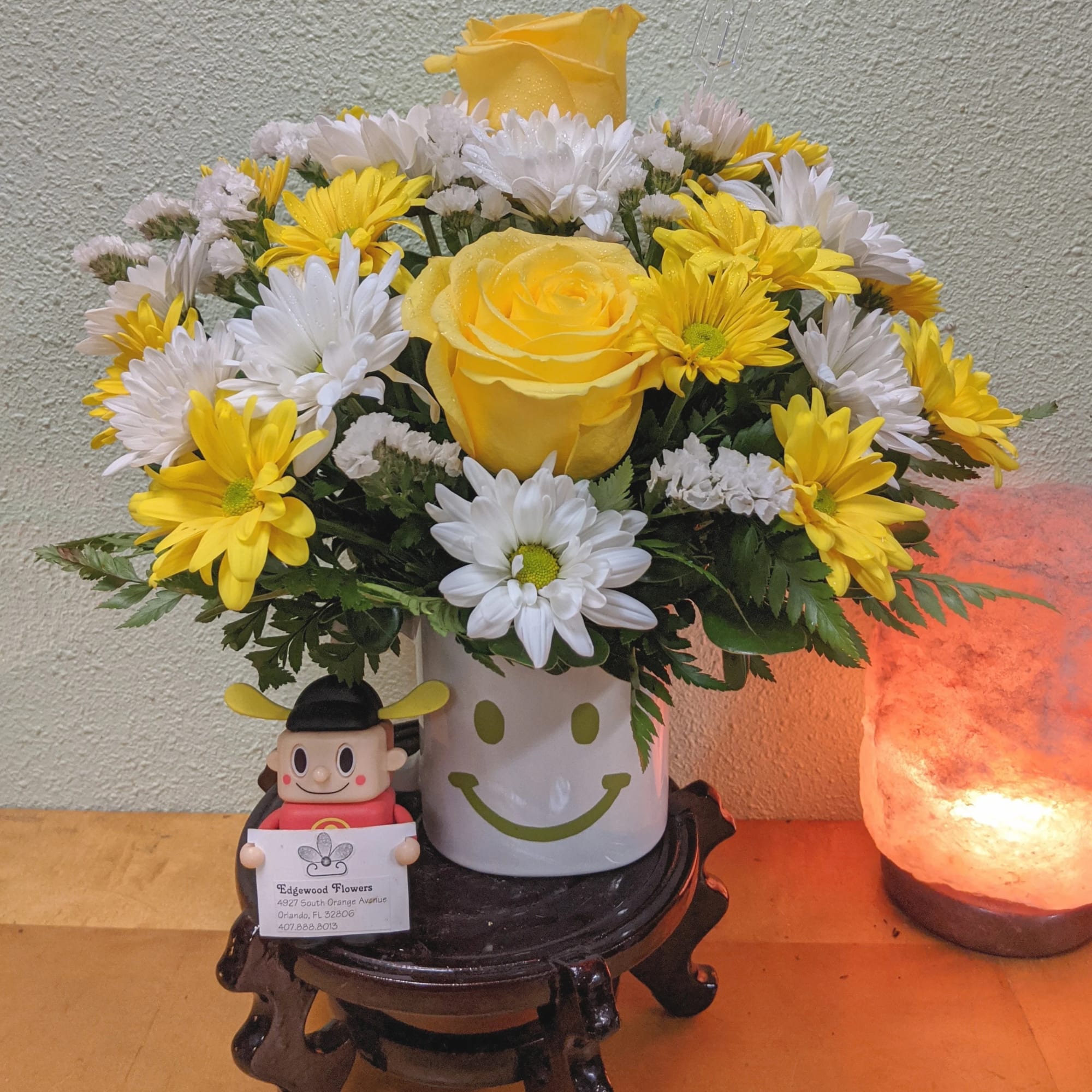 Yellow roses and white daisies in a smiley-face mug with a small figurine