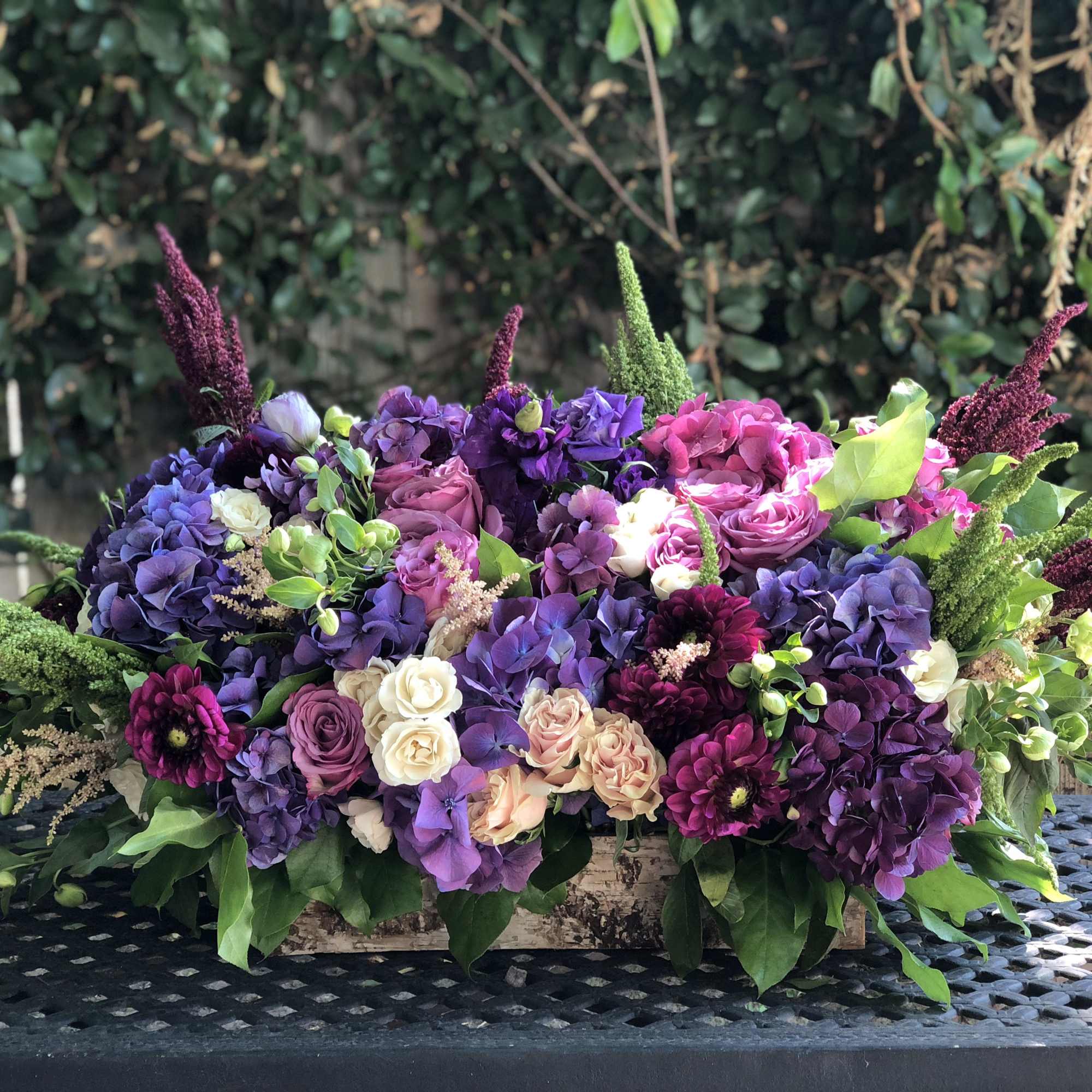 Low floral arrangement of purple, pink, and white blooms in a wooden box