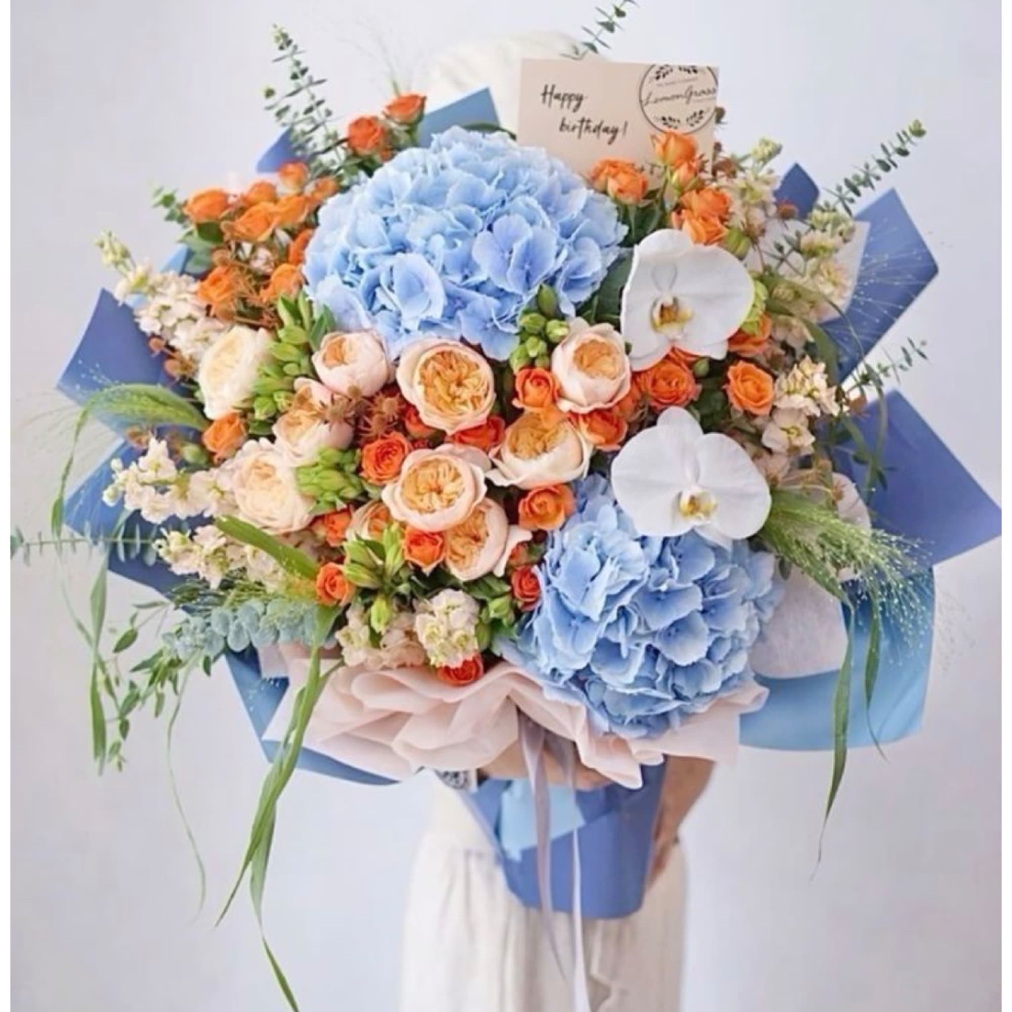 Large bouquet of blue hydrangeas, orange roses, and white orchids with a birthday card
