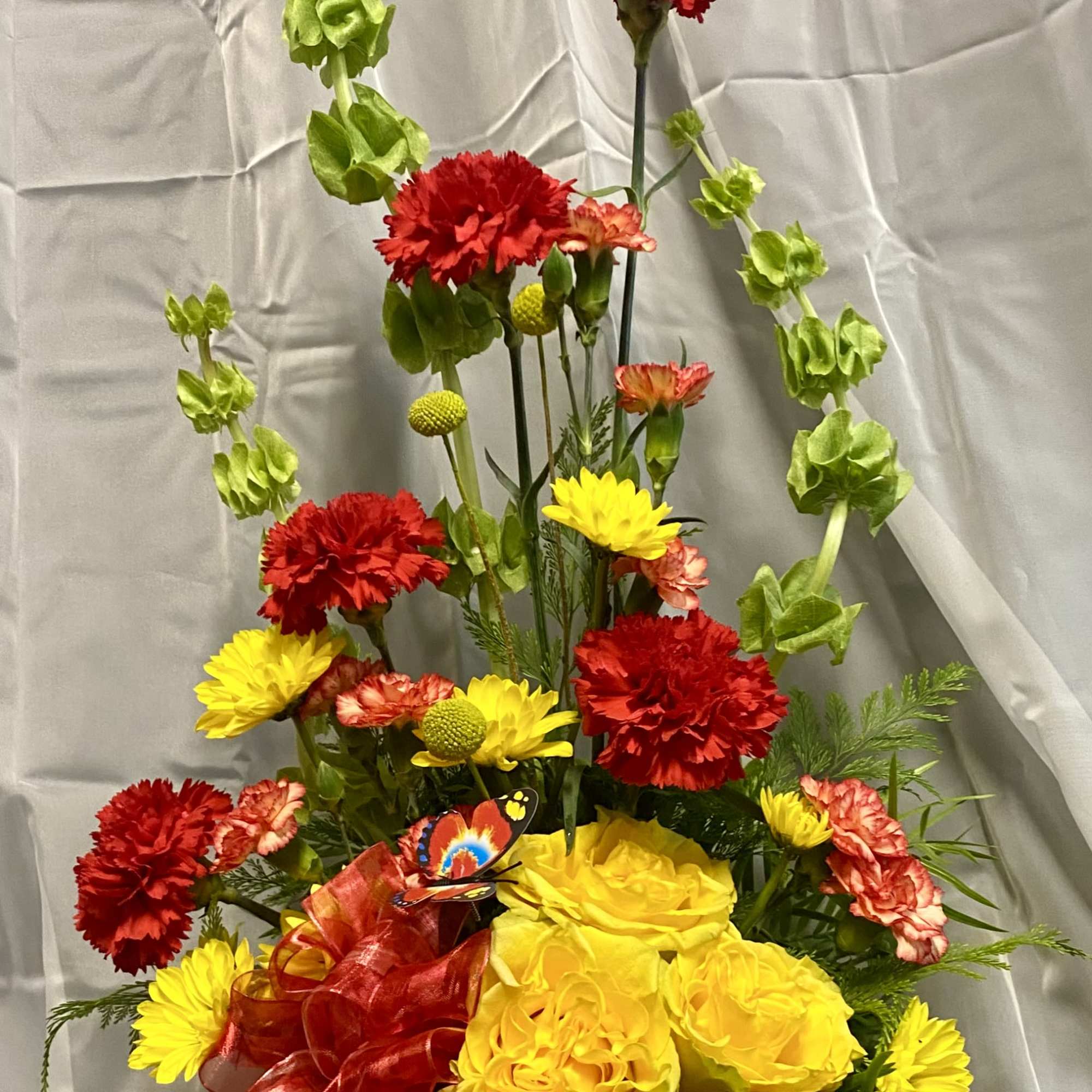Yellow and red floral arrangement in a round container with a red ribbon