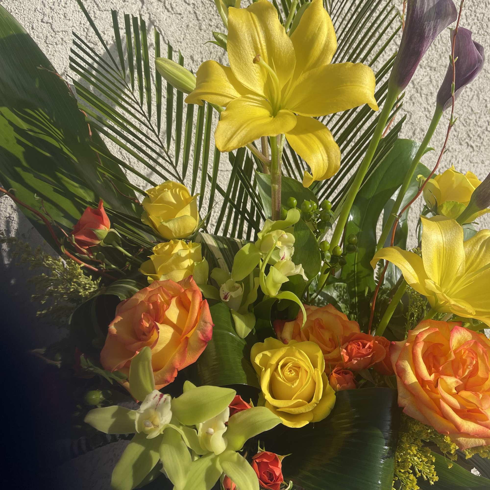 Tall arrangement of yellow lilies, roses, green orchids, and purple calla lilies in a wooden box