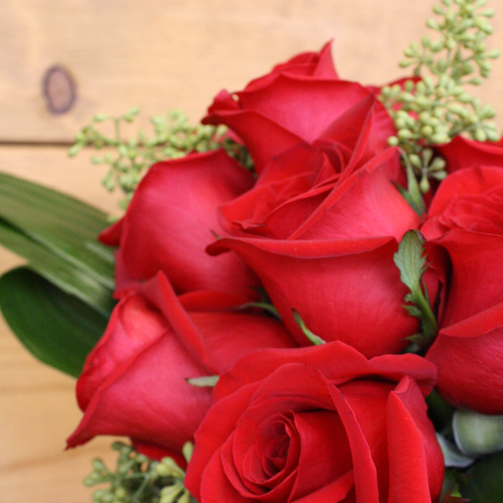 Bouquet of red roses with green filler on a wooden background