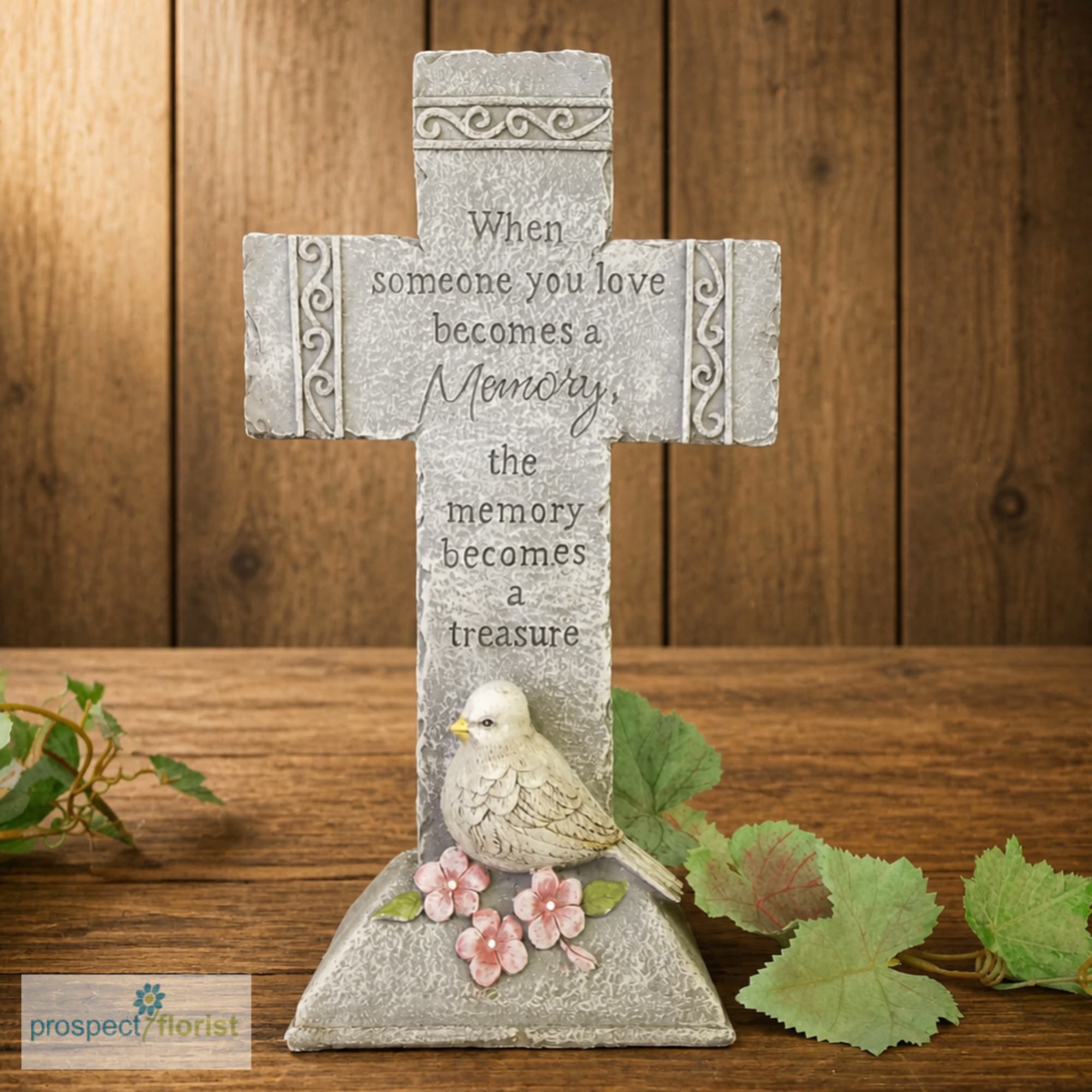 Decorative memorial cross with a bird and pink flowers on a wooden surface