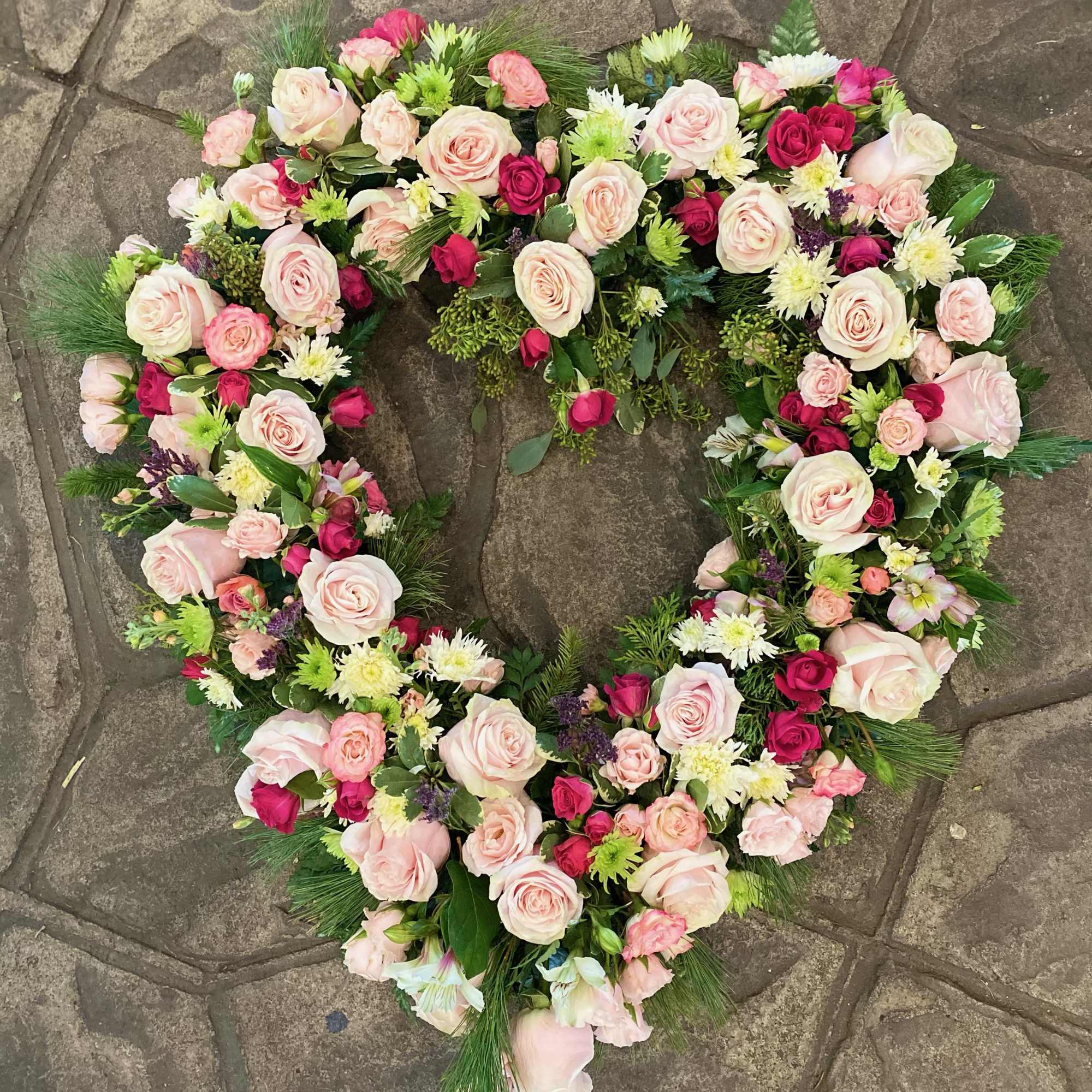 Heart-shaped floral wreath with pink and white roses on a stone surface