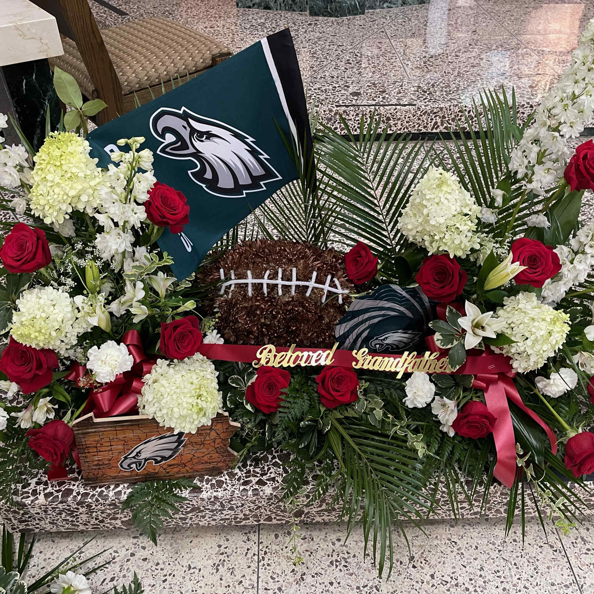 Floral funeral tribute with red roses, white blooms, and an Eagles football theme