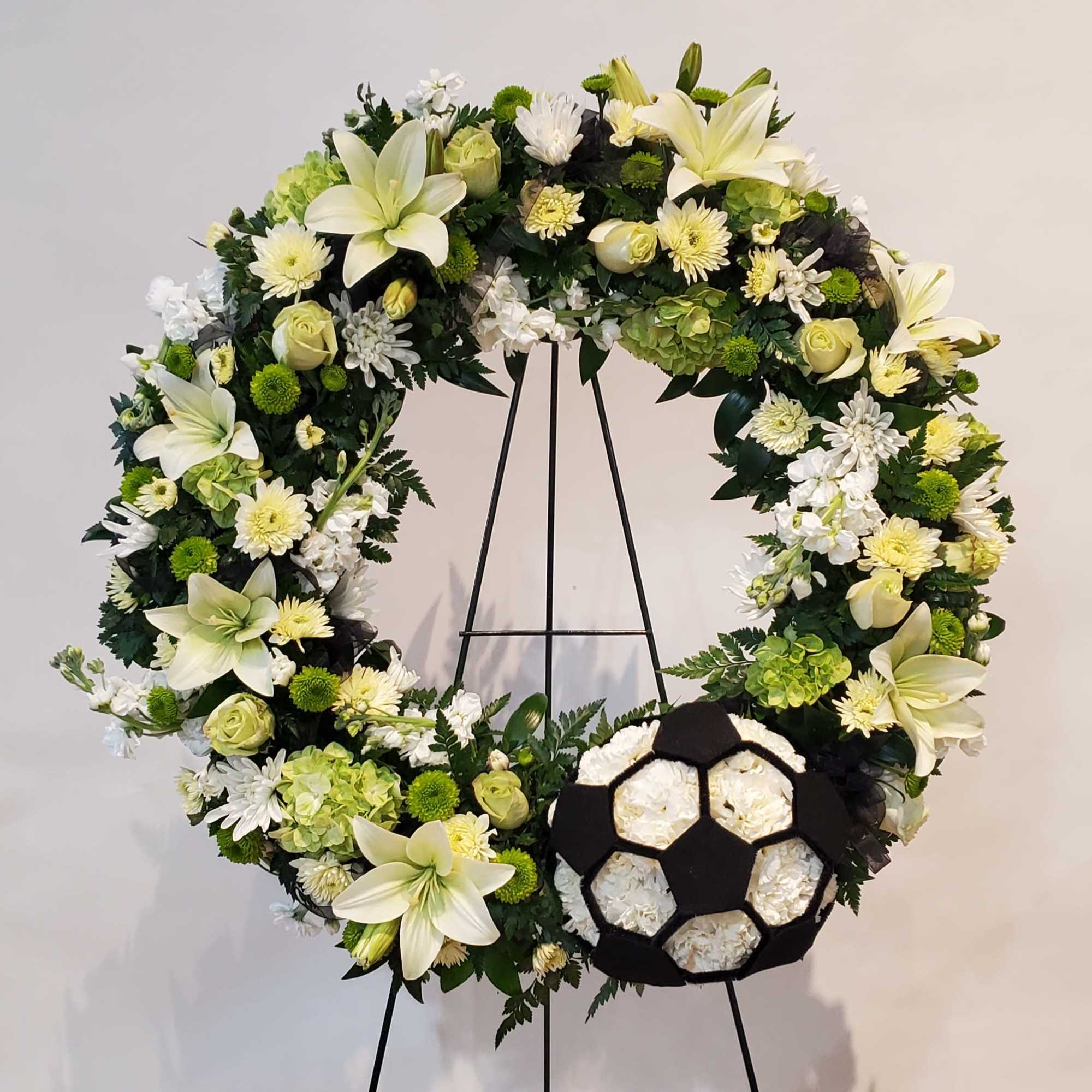 Large white and green floral wreath on a black stand with a soccer ball accent