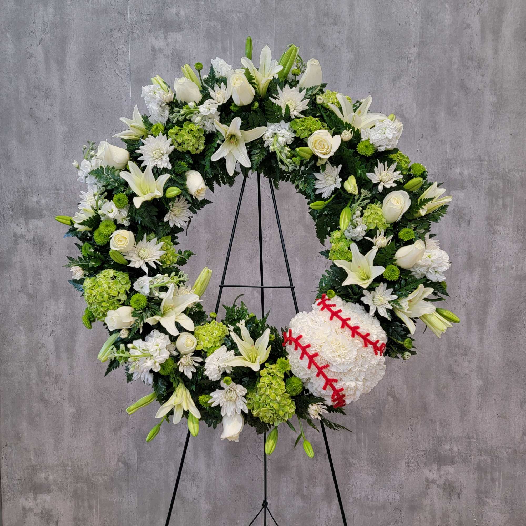 White floral wreath on a stand with a baseball at the lower right