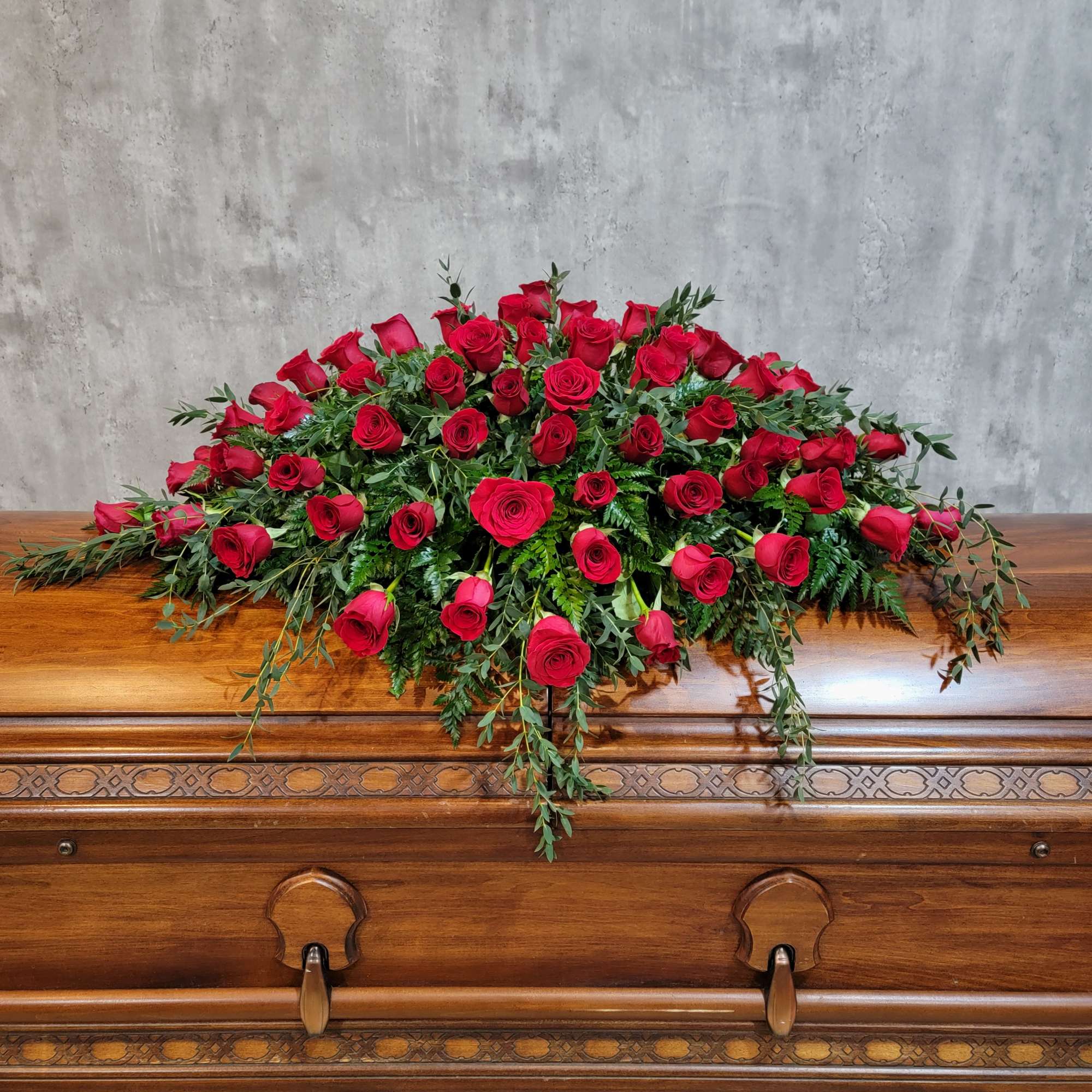 Red rose casket spray with trailing greenery on a wooden casket