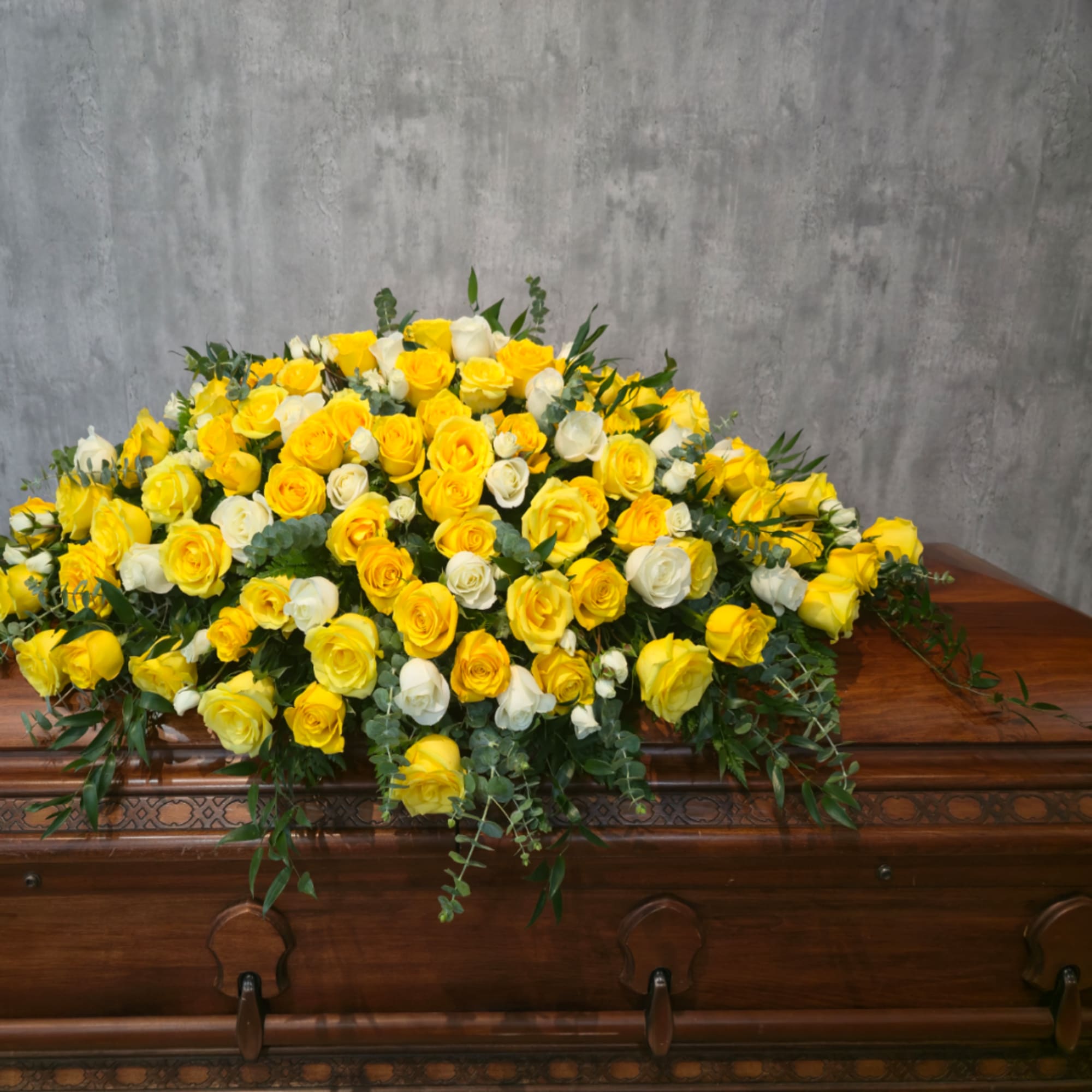 Large yellow and white rose arrangement on a wooden casket