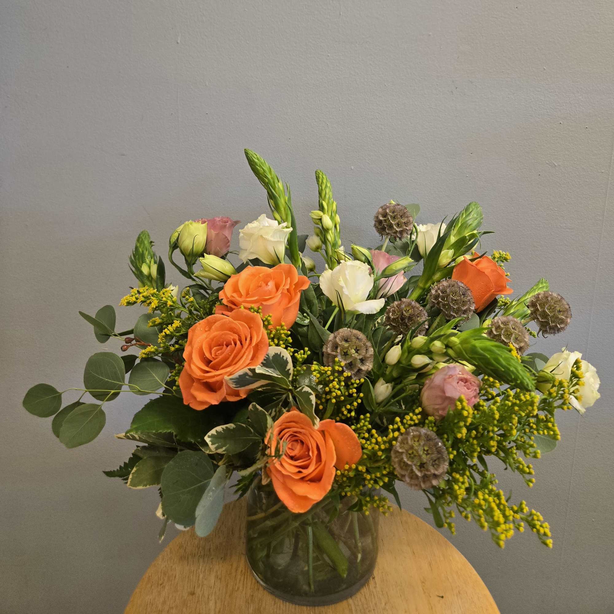 Bright orange roses take center stage in this garden-style flower arrangement, a