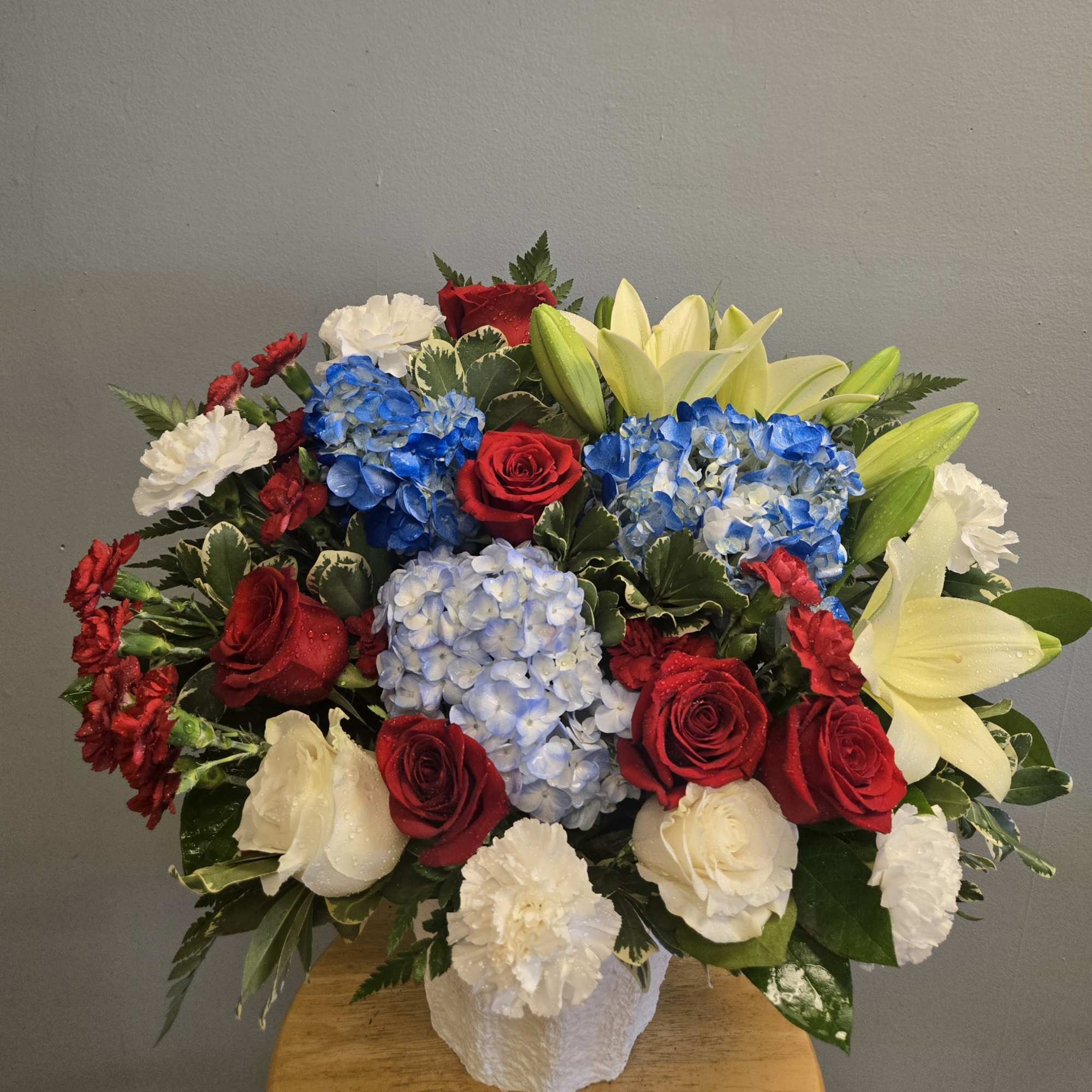 Red roses, blue hydrangeas, white lilies, and carnations in a white vase