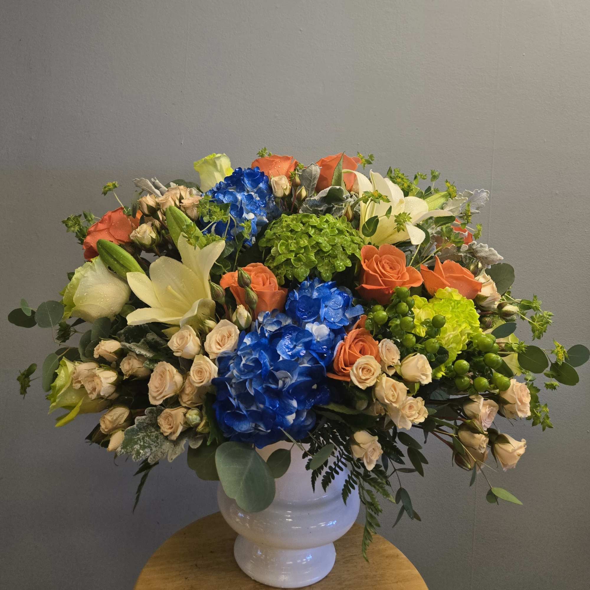 Large mixed bouquet in a white vase with blue, orange, cream, and green blooms