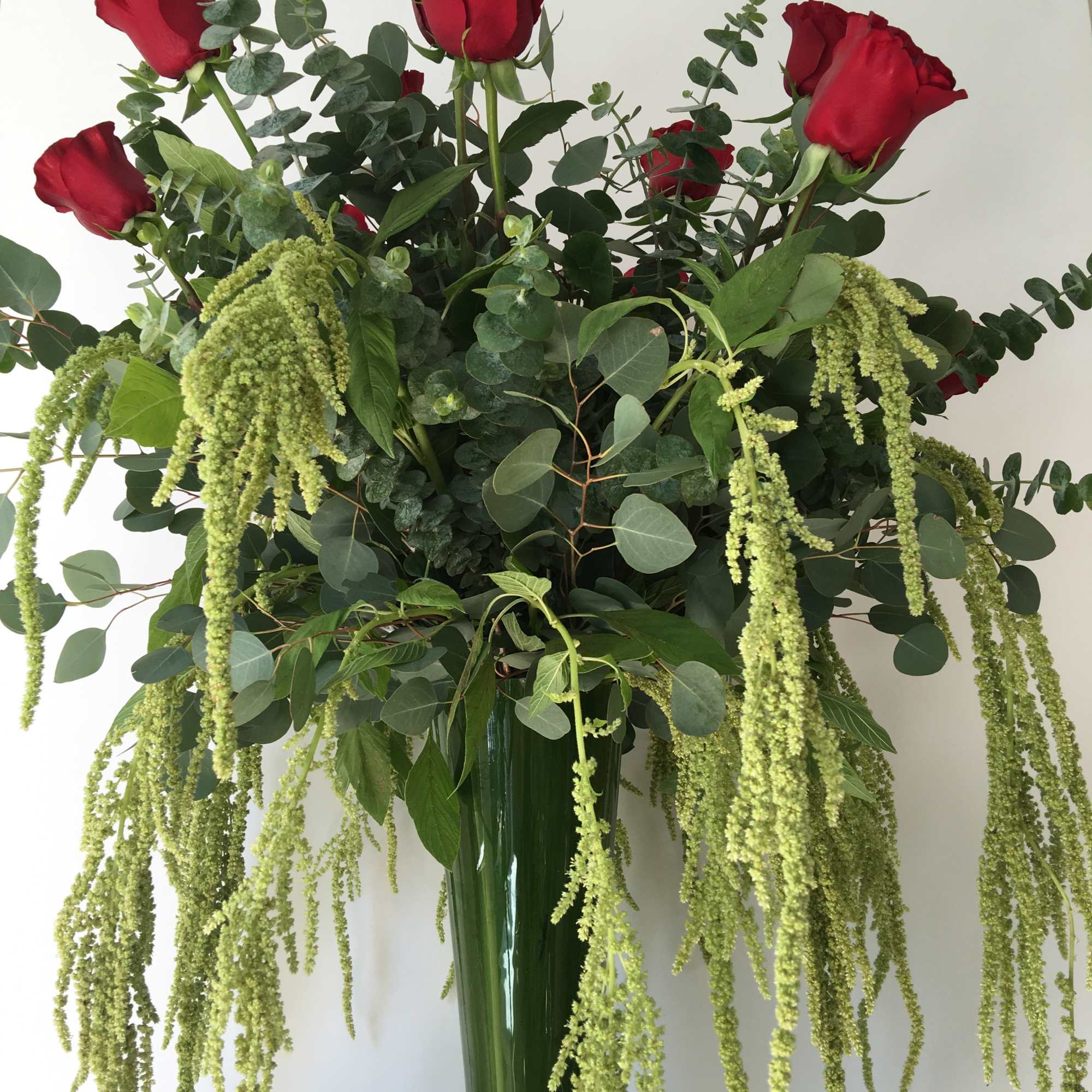 Tall bouquet of red roses and trailing green amaranthus in a glass vase