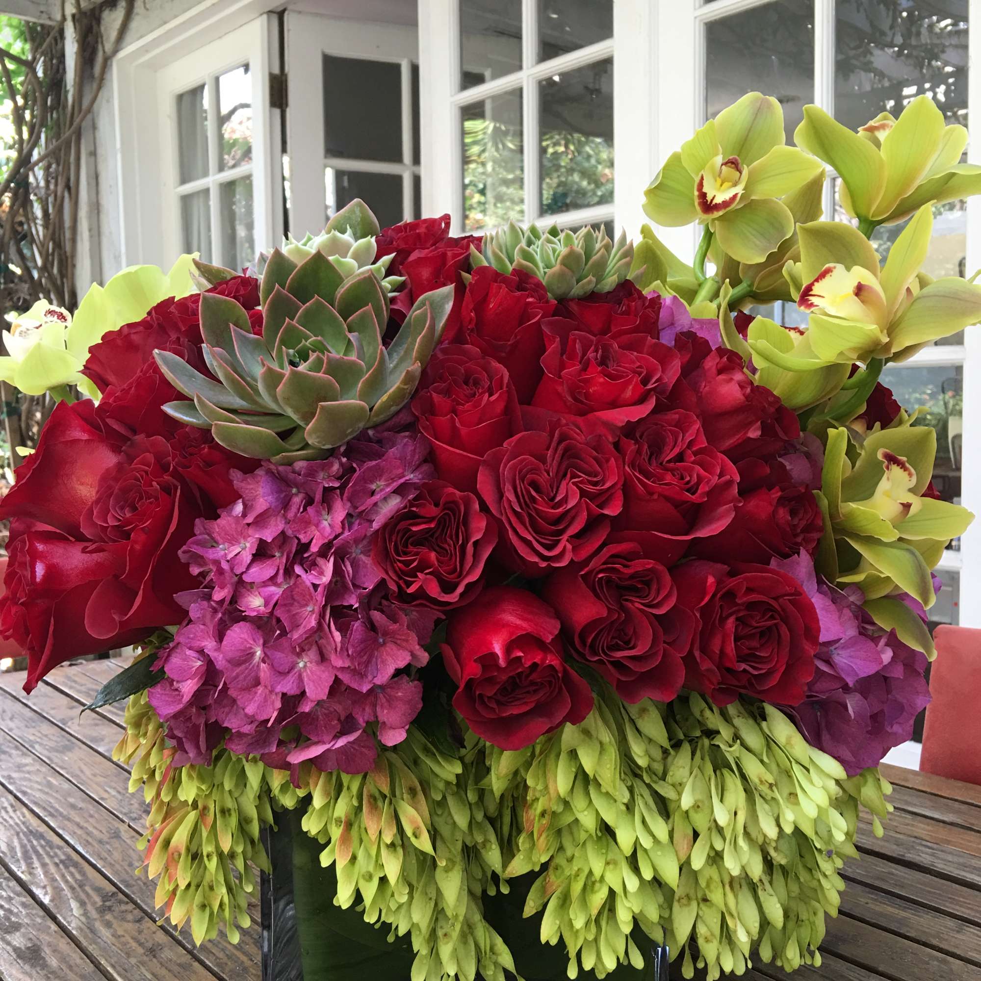 Red roses, purple hydrangeas, and green orchids in a square vase