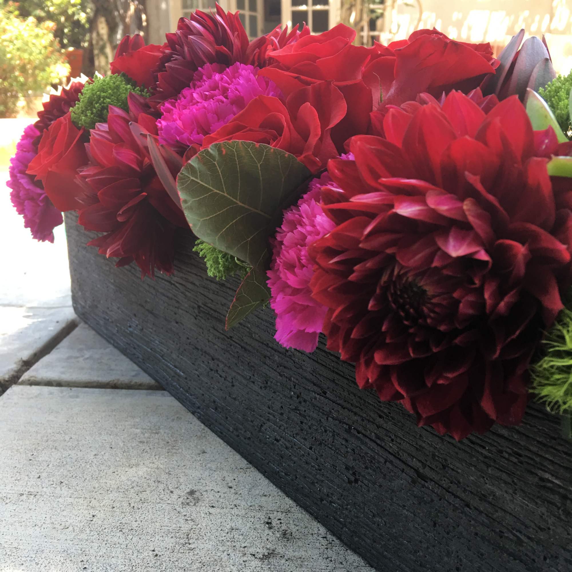 Red and magenta floral arrangement in a black rectangular planter