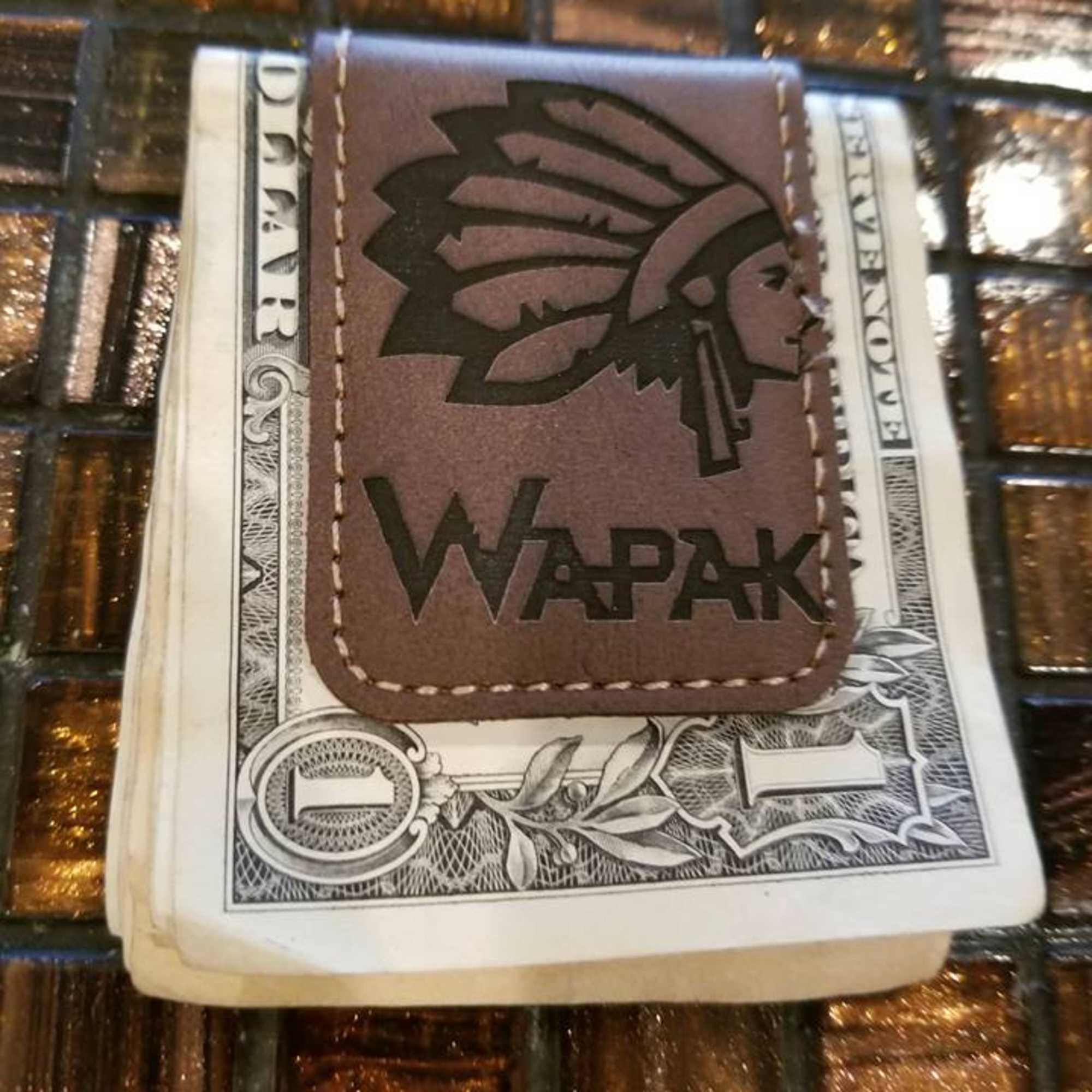 A stack of U.S. dollar bills with a leather WAPAK card holder on top