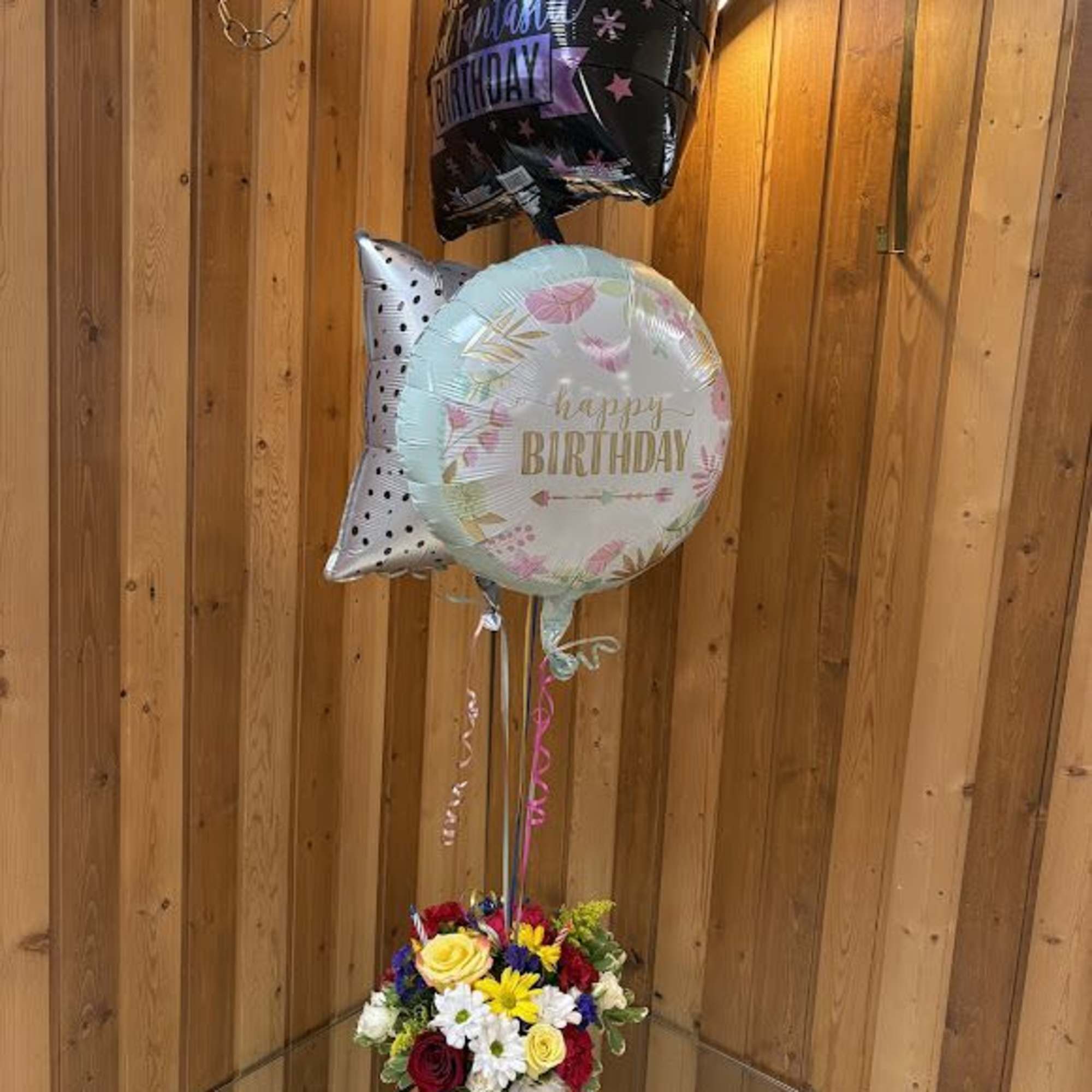 Birthday balloons above a colorful flower arrangement in a vase.