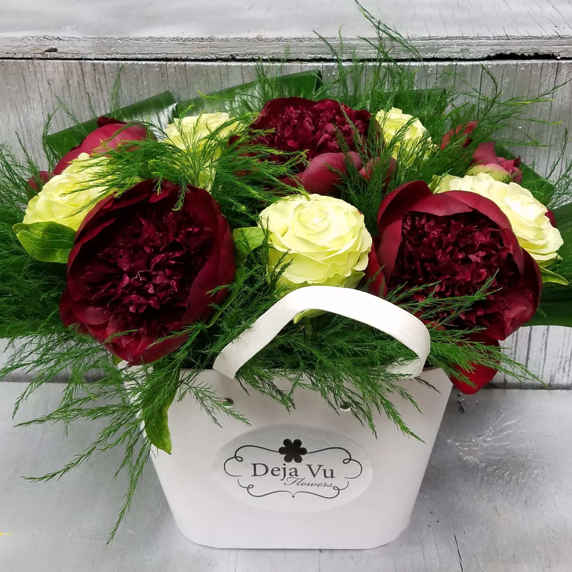 Red and cream roses arranged in a white box with greenery